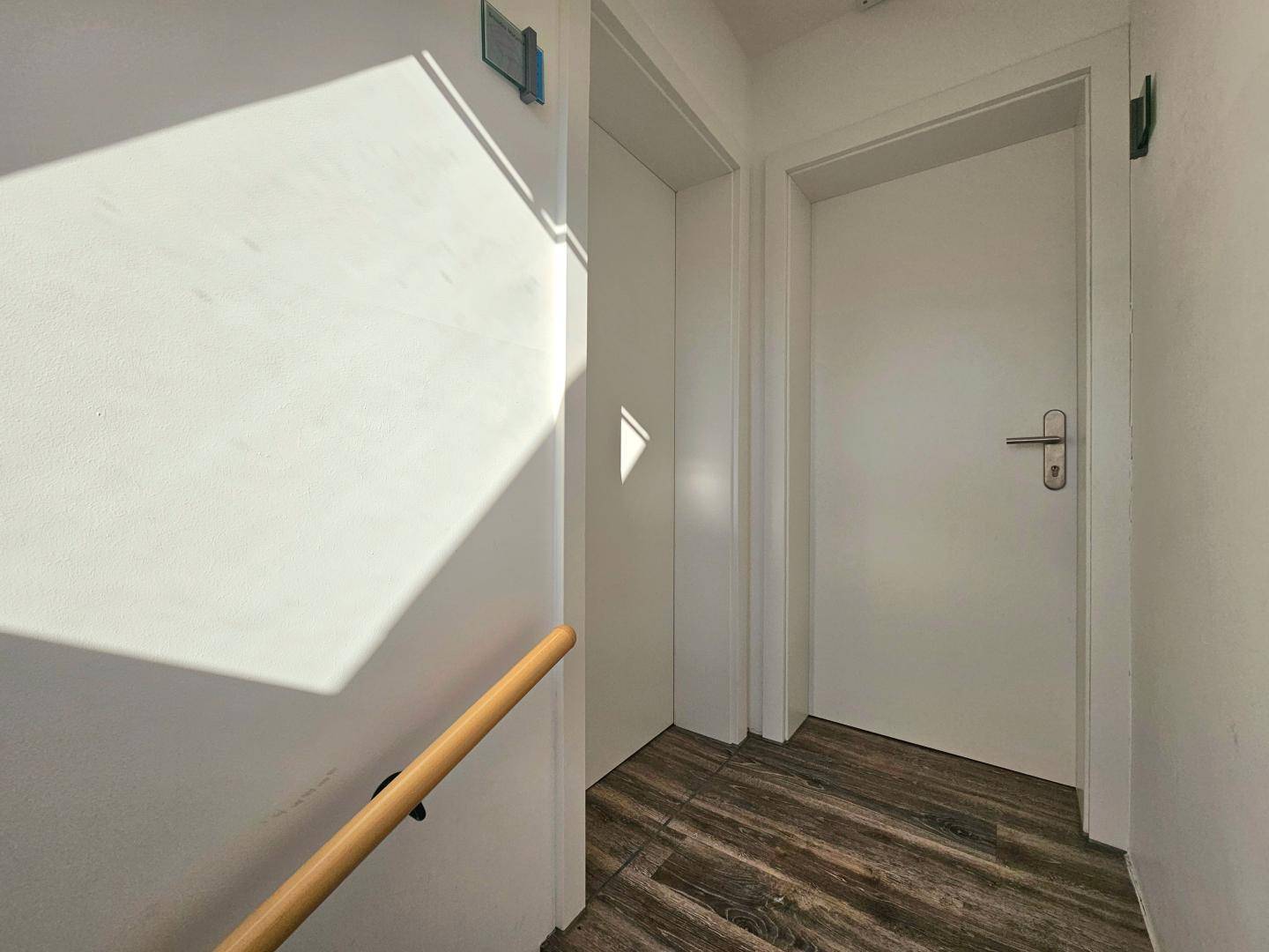 Heller Flur mit Laminatboden und zwei weißen Türen, die zu den Zimmern führen.
