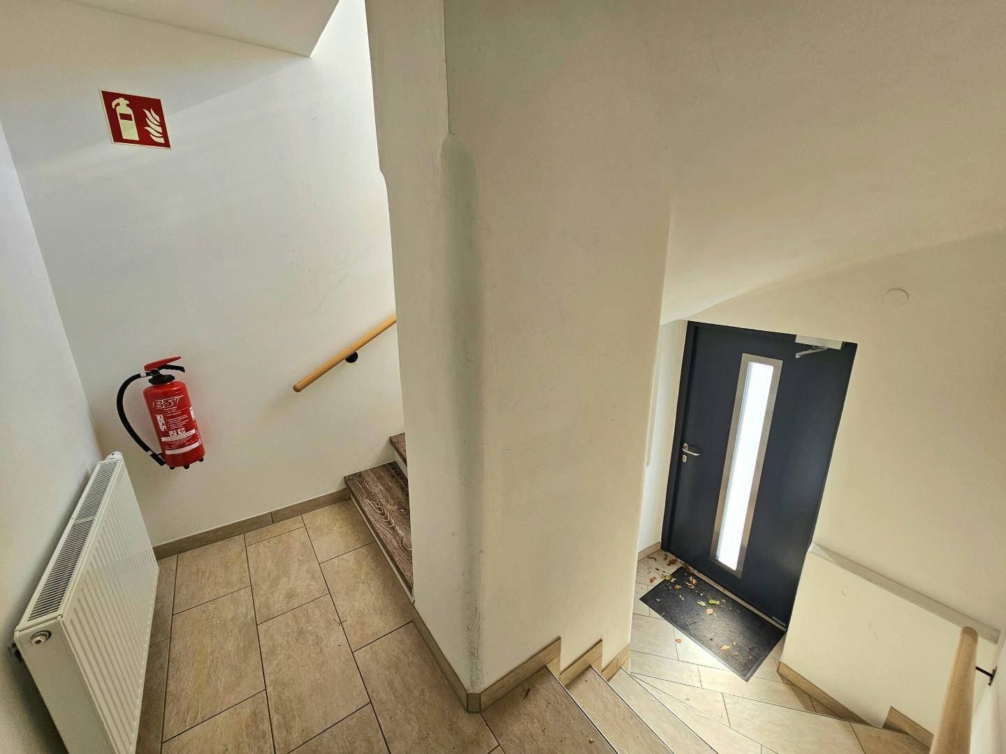 Heller Eingangsbereich mit Treppe, Fliesenboden und Brandschutzvorrichtungen.