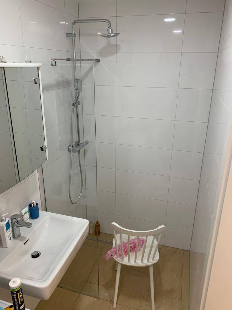 Modernes Badezimmer mit ebenerdiger Dusche, Waschbecken und weißen Fliesen.