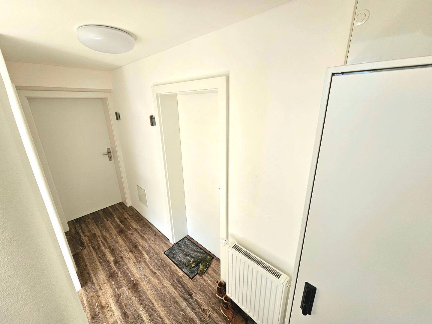 Heller Flur mit Laminatboden, Heizkörper und weißen Türen.