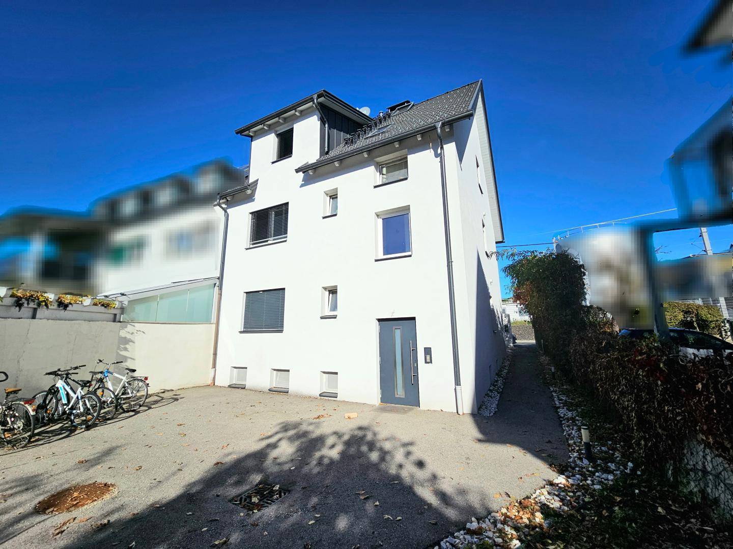 Modernes weißes Mehrfamilienhaus mit Parkplatz und Fahrrädern im Vordergrund.