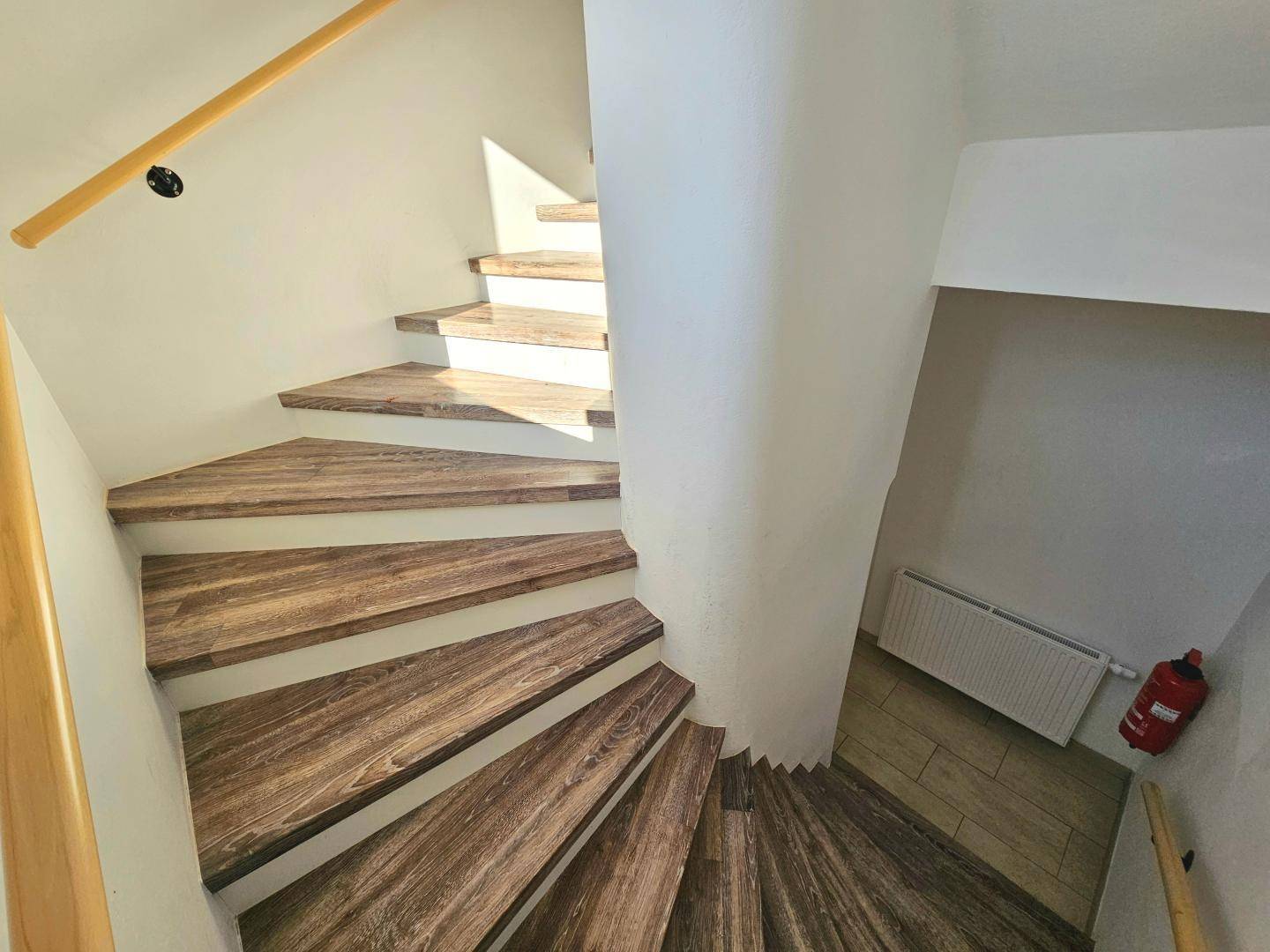 Holztreppe mit hellem Geländer in einem gut beleuchteten Treppenhaus.