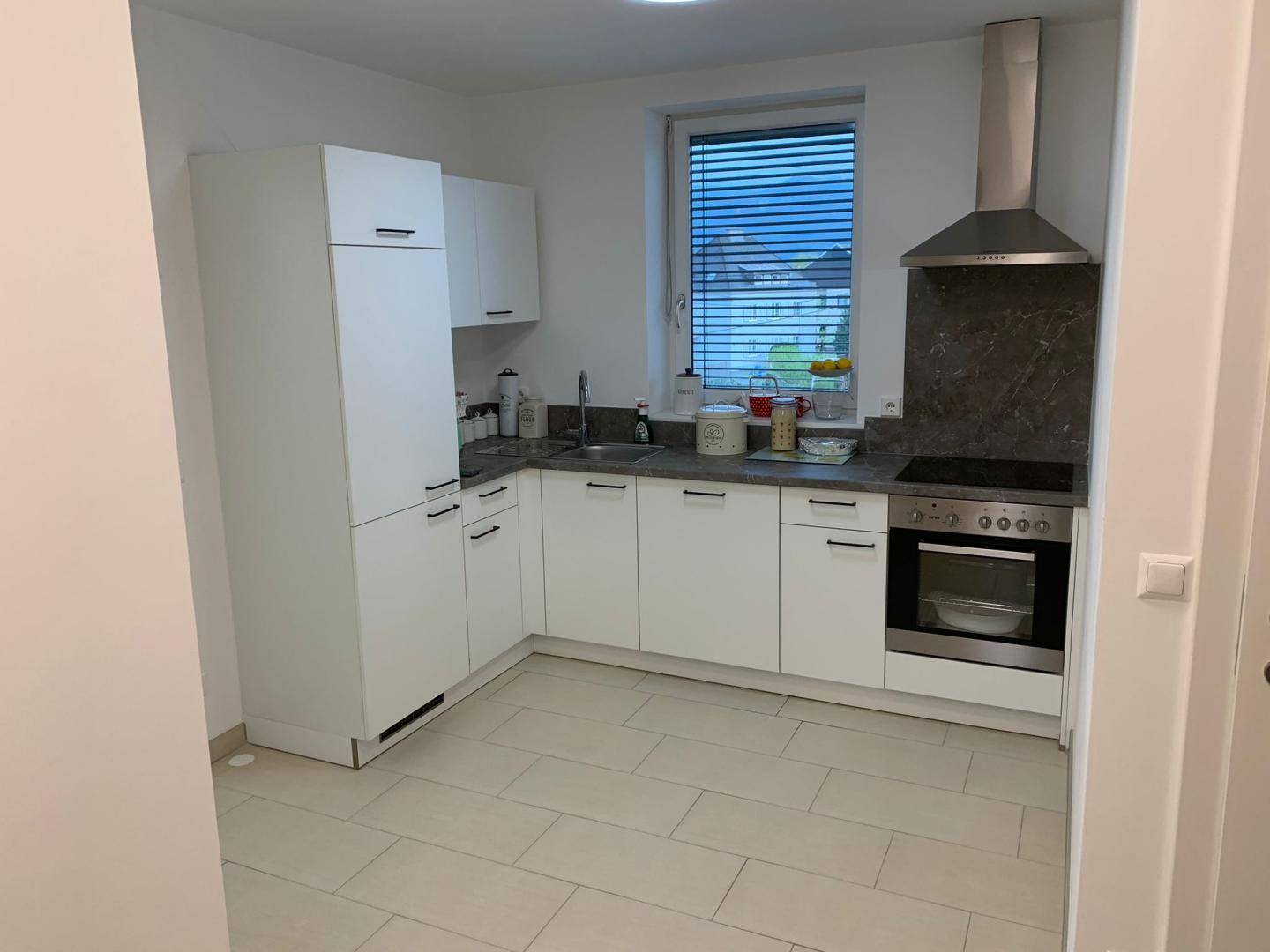 Moderne Einbauküche mit weißen Schränken, Fliesenboden und Fenster.