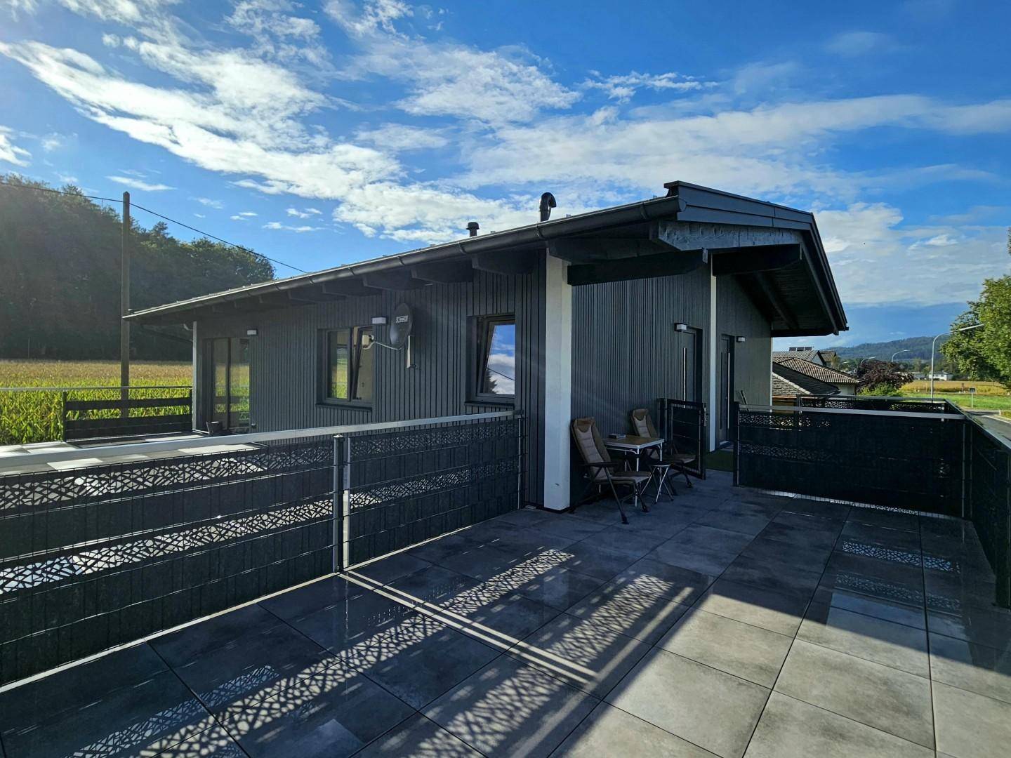 Sonnige Dachterrasse mit modernen Fliesen, bequemen Sitzgelegenheiten und Blick ins Grüne.