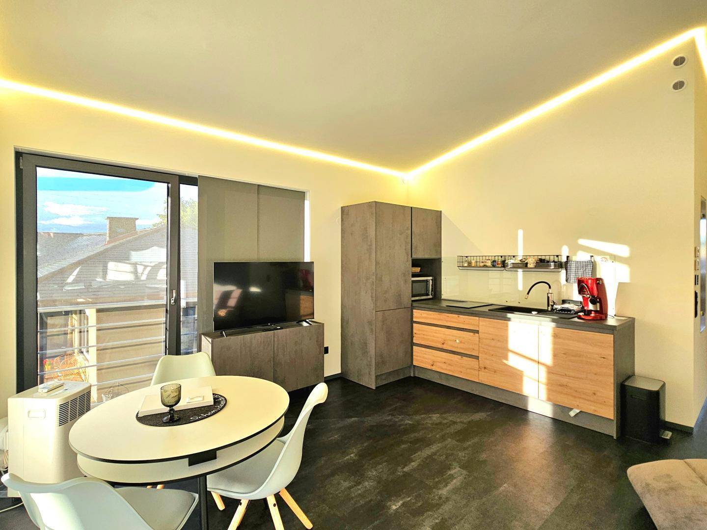 Moderne Küchenzeile mit integrierten Geräten, Essbereich und Zugang zum Balkon.