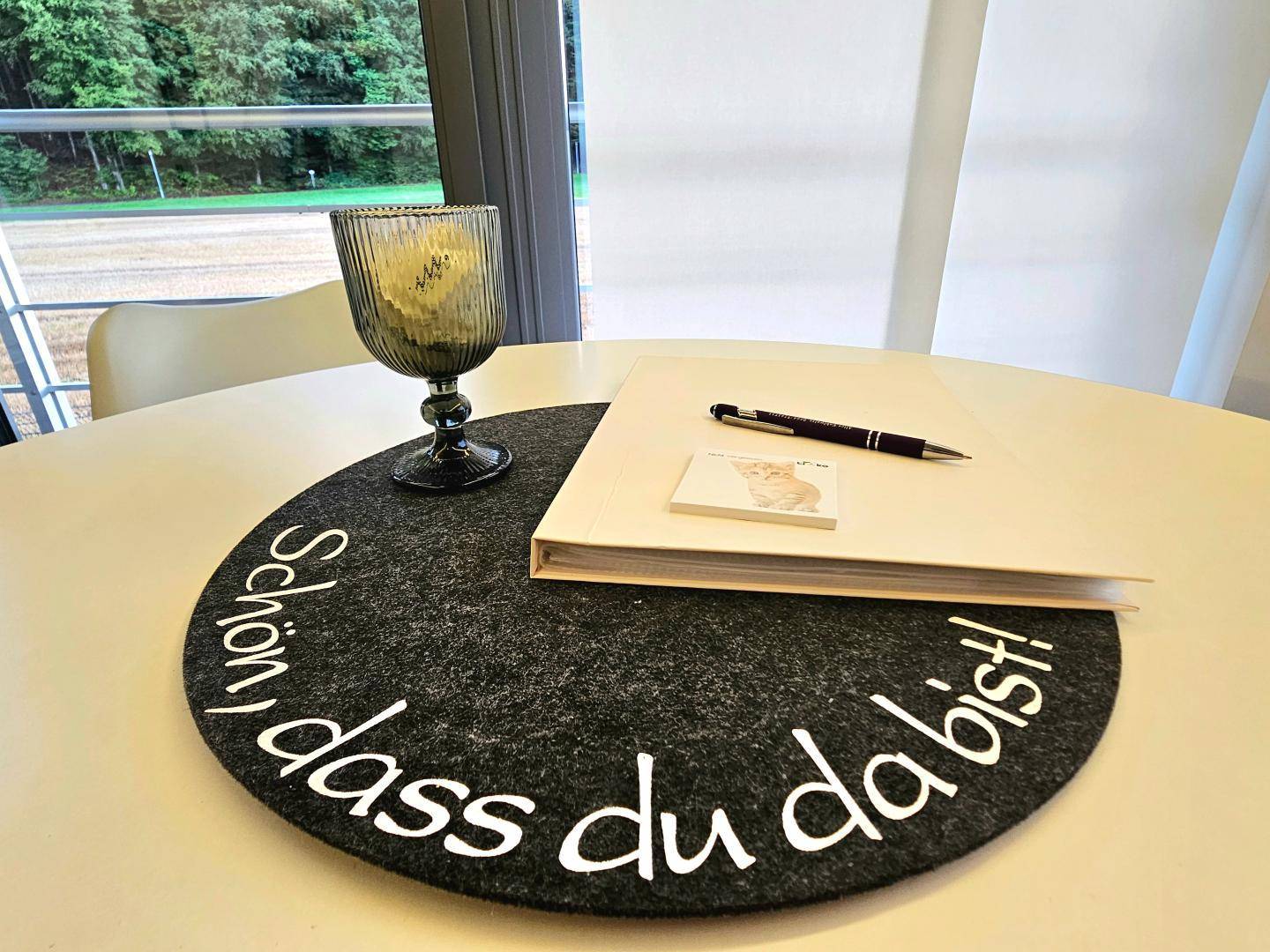 Detailaufnahme eines Esstisches mit Dekoration und einem Glas, im Hintergrund Grünblick.