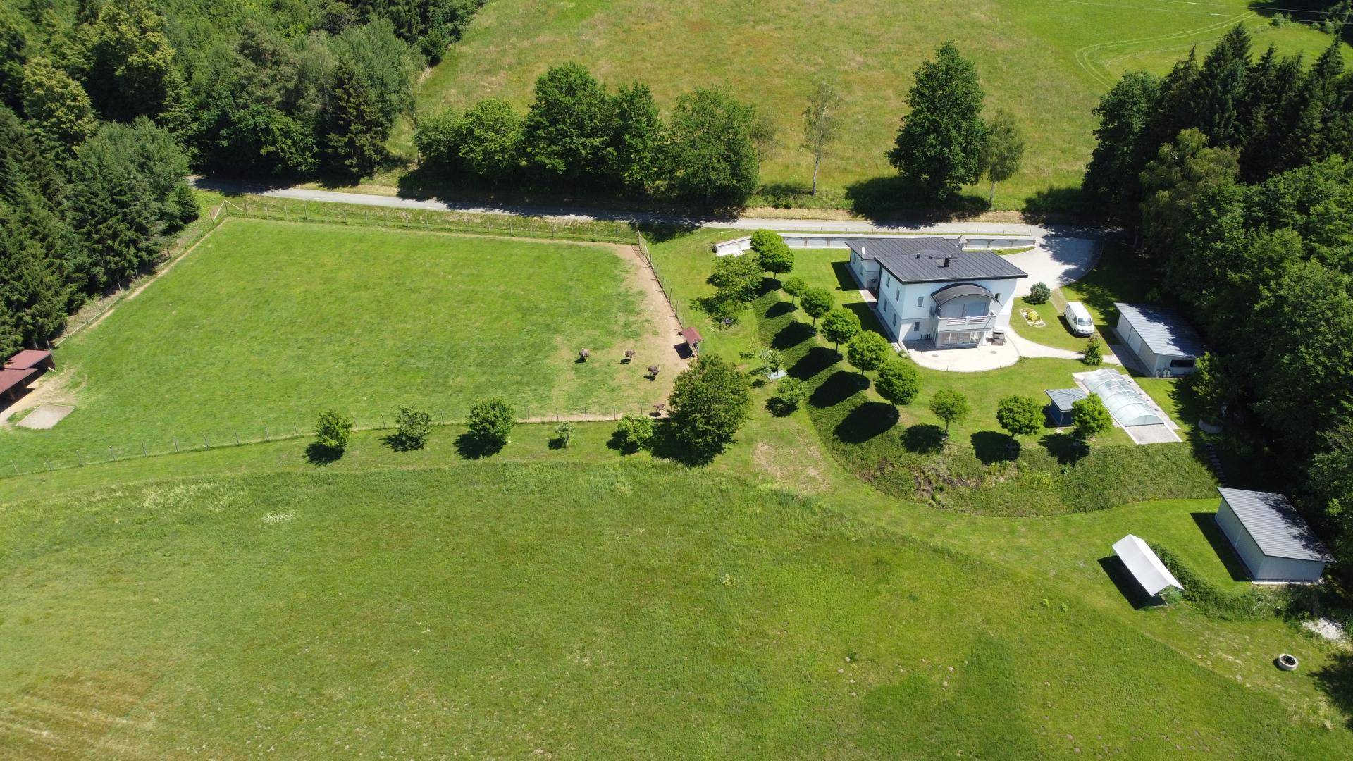 Weitläufige Luftaufnahme des Anwesens mit Wohnhaus, großem eingezäunten Feld und umgebender Natur.