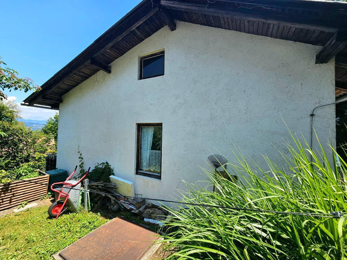 Seitenansicht des Hauses mit Gartenbereich, hohen Gräsern und Blick auf die Landschaft.