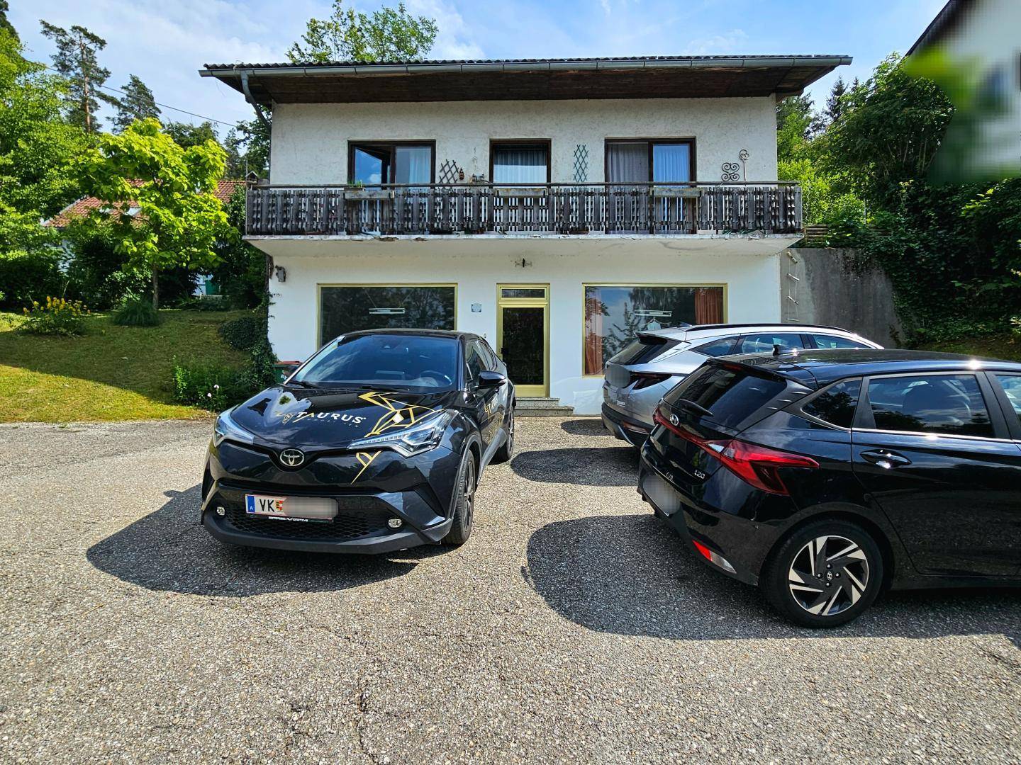 Vorderansicht des Hauses mit geparkten Autos und einem Balkon im Obergeschoss.