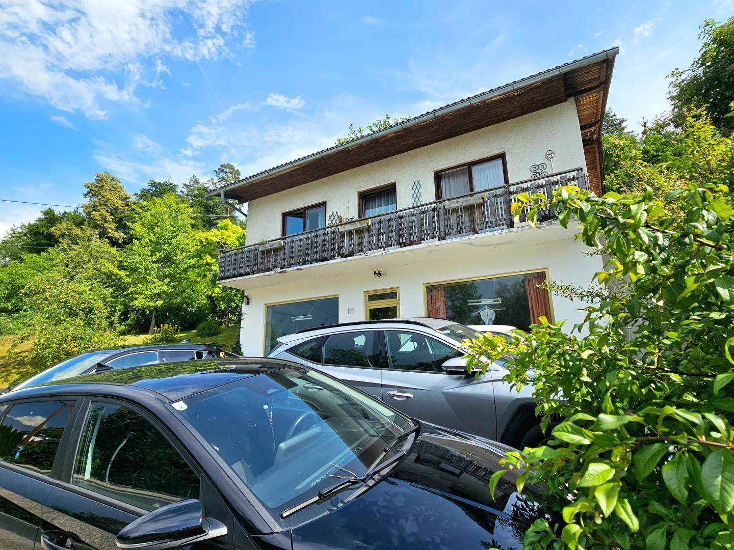 Seitenansicht des Gebäudes mit Balkon und umgebender grüner Natur unter blauem Himmel.