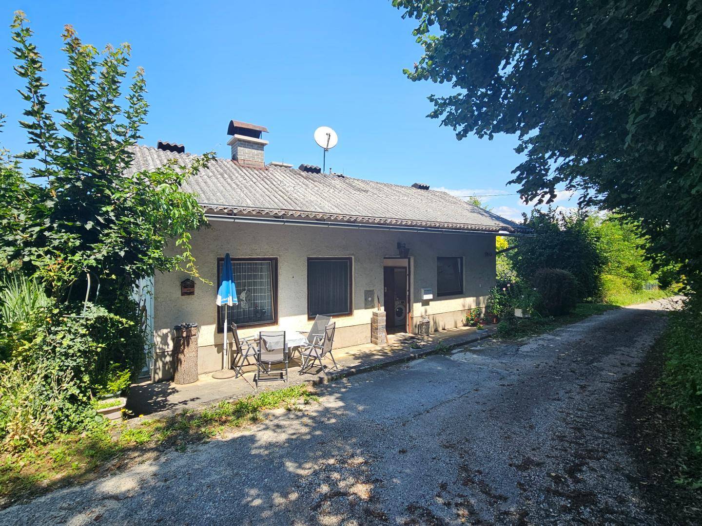 Außenansicht des Hauses mit Terrasse und einem Schotterweg, umgeben von Bäumen.