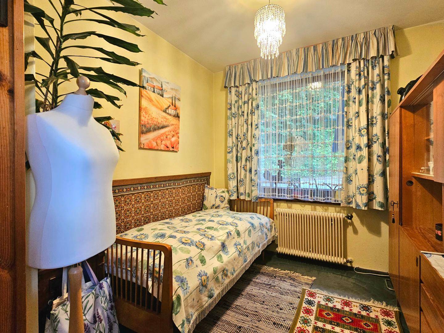 Gemütliches Schlafzimmer mit Einzelbett, gelben Wänden und traditionellen Vorhängen am Fenster.