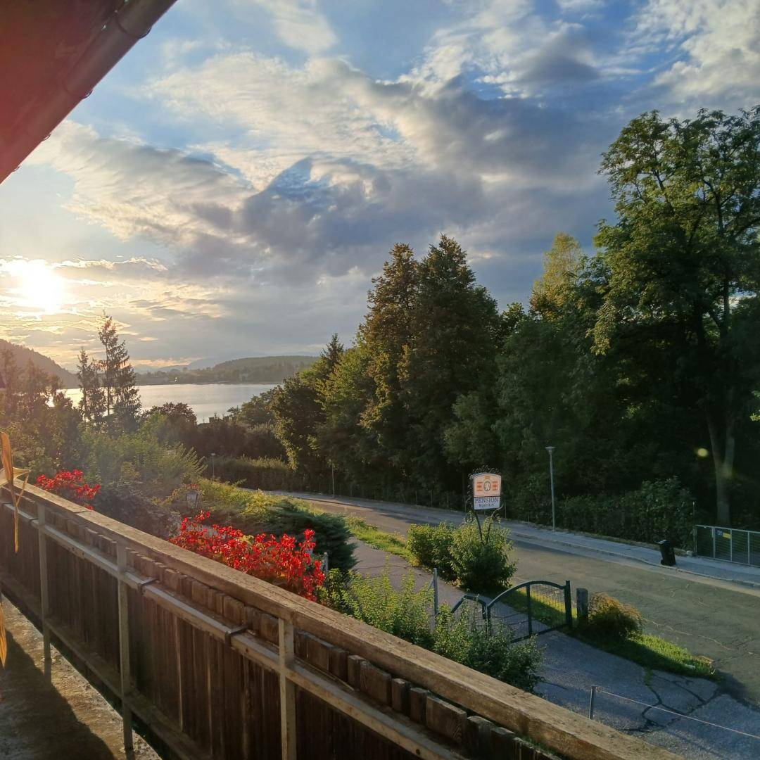 Balkon mit Blick auf den See bei Sonnenuntergang, umgeben von üppigem Grün und Bäumen.