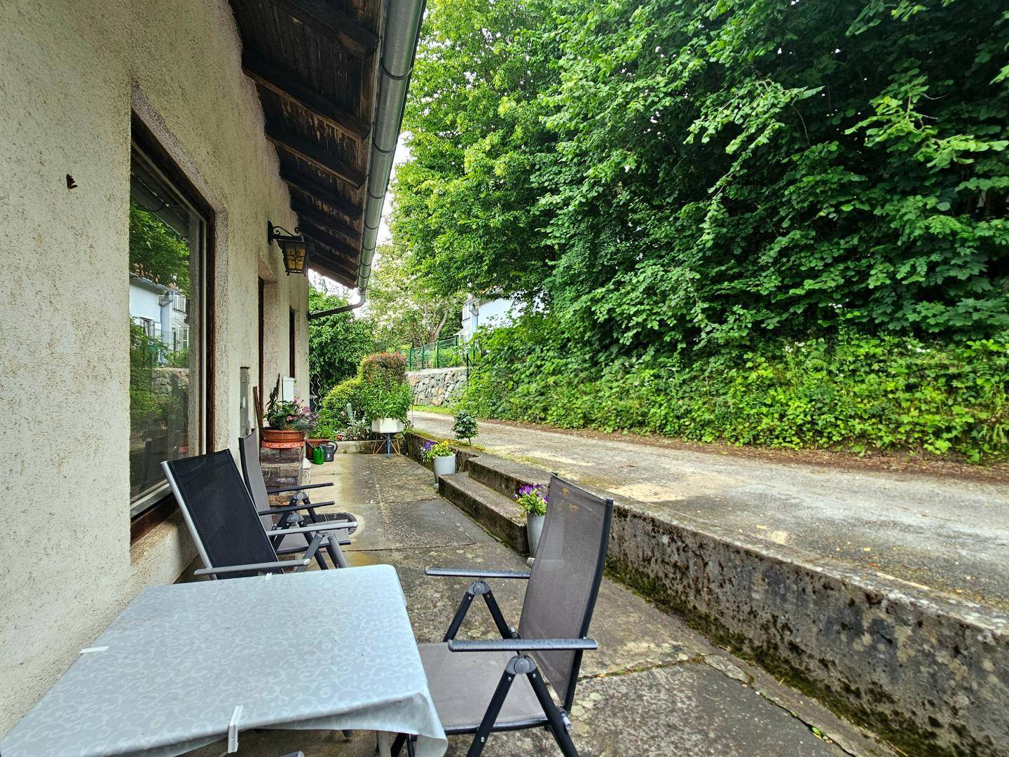 Gemütliche Terrasse mit Gartenmöbeln und Blick auf die grüne Umgebung und einen Weg.