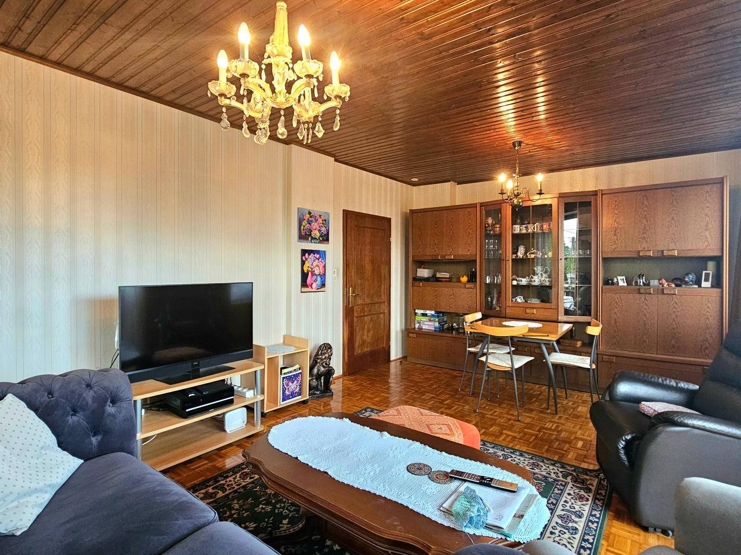 Wohnbereich mit Holzbalkendecke, Parkettboden, Fernseher und einem Esstisch.