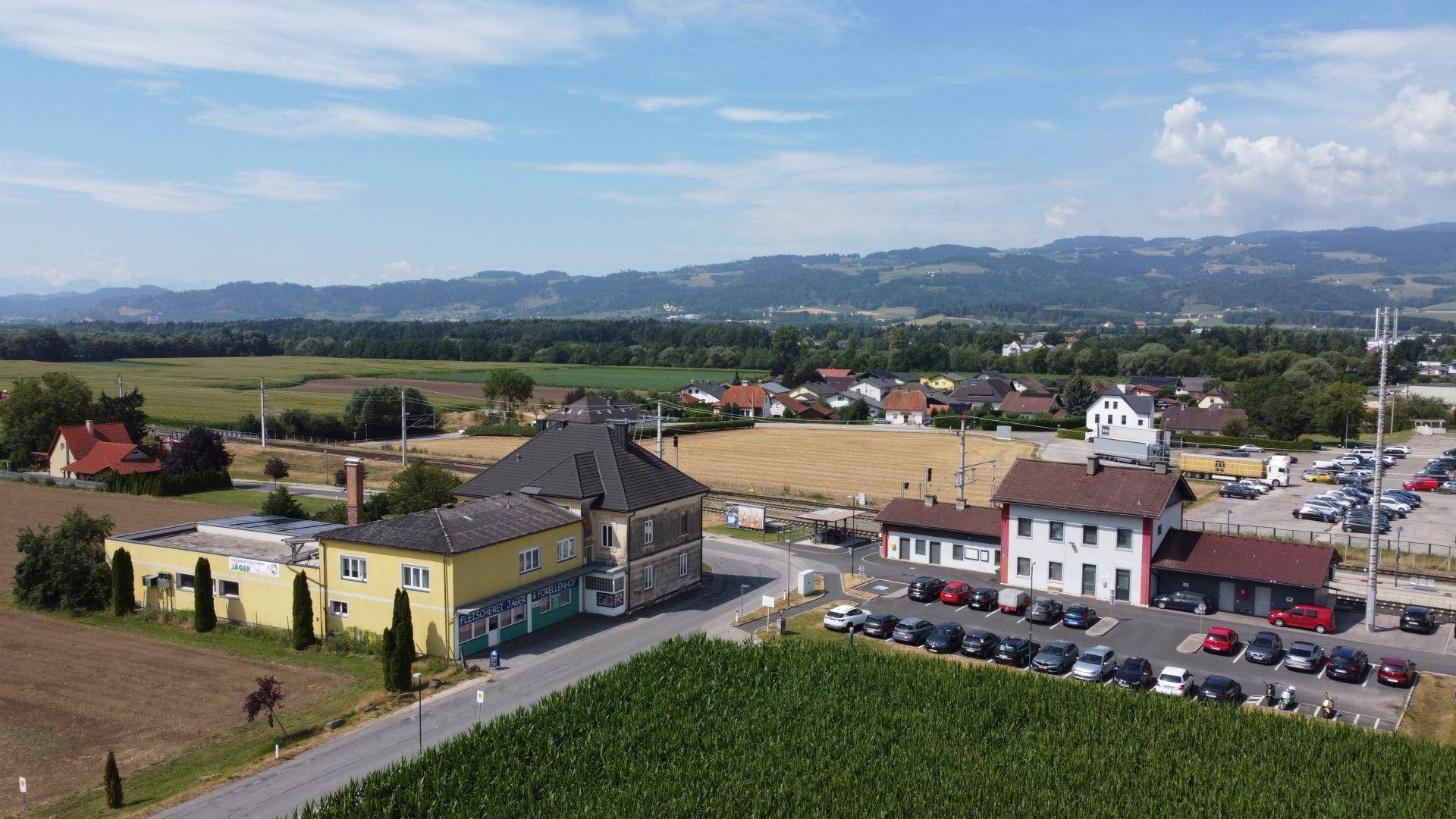 Weitläufige Luftaufnahme des Anwesens mit Bahngleisen, Feldern und einer Bergkette am Horizont.