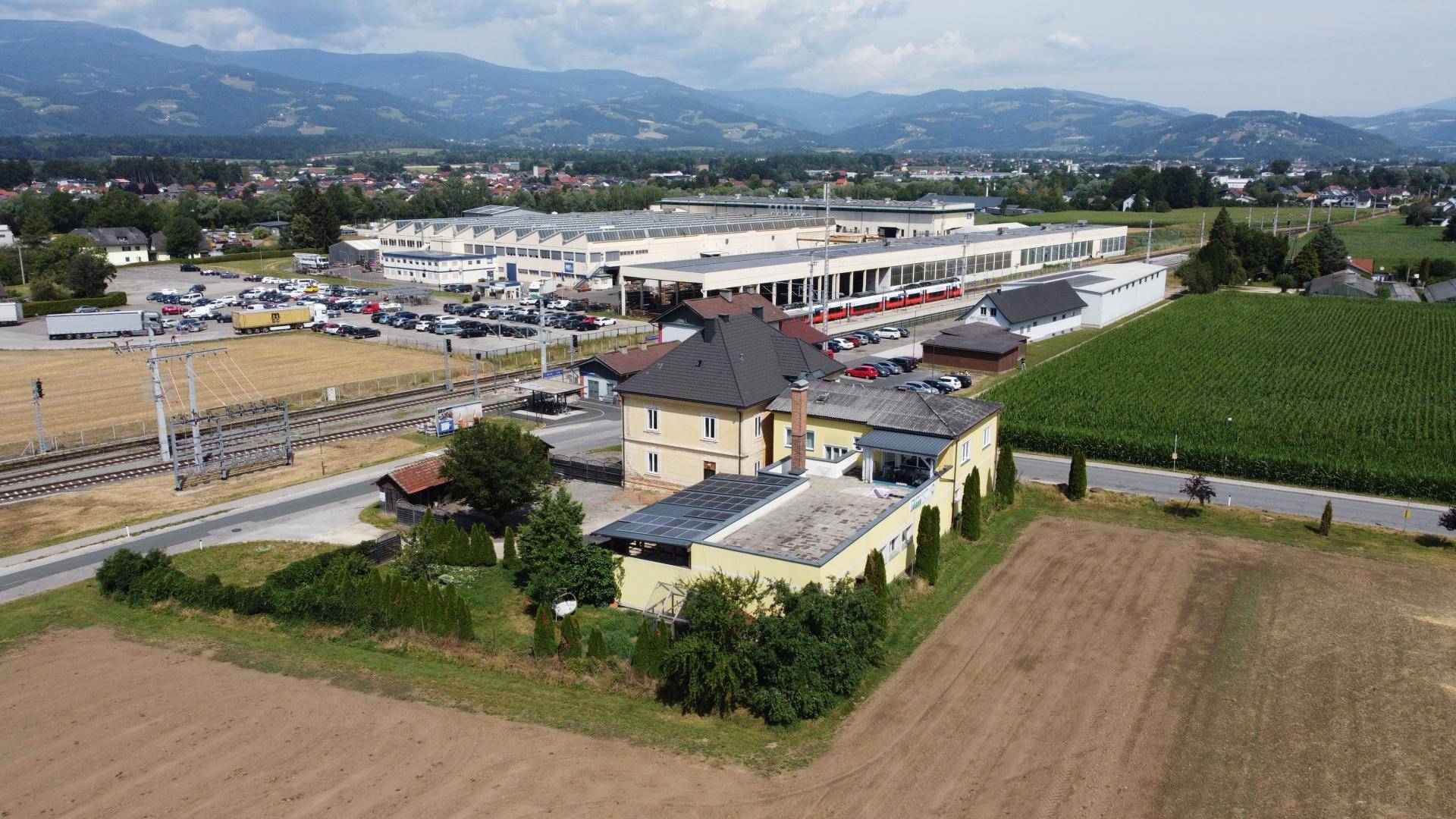Panoramablick aus der Luft auf das Gebäude, umgeben von Feldern, Bahngleisen und einer Industrieanlage.