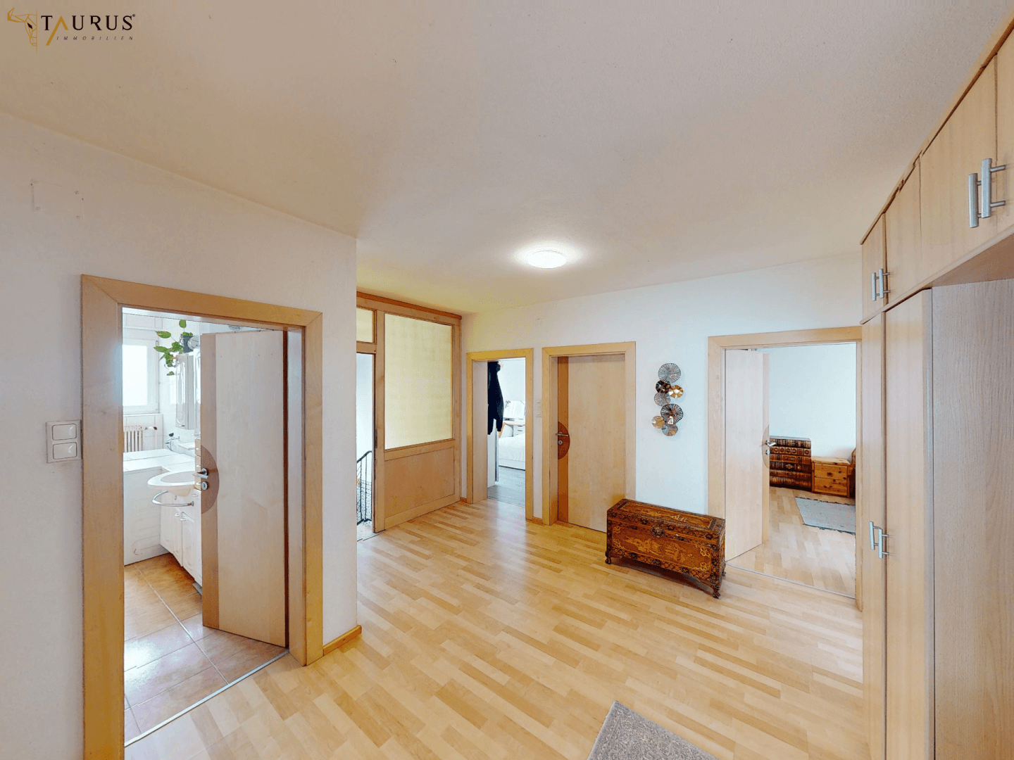 Heller Flur mit Holzfußboden, mehreren Türen und einem dekorativen Holzkasten.