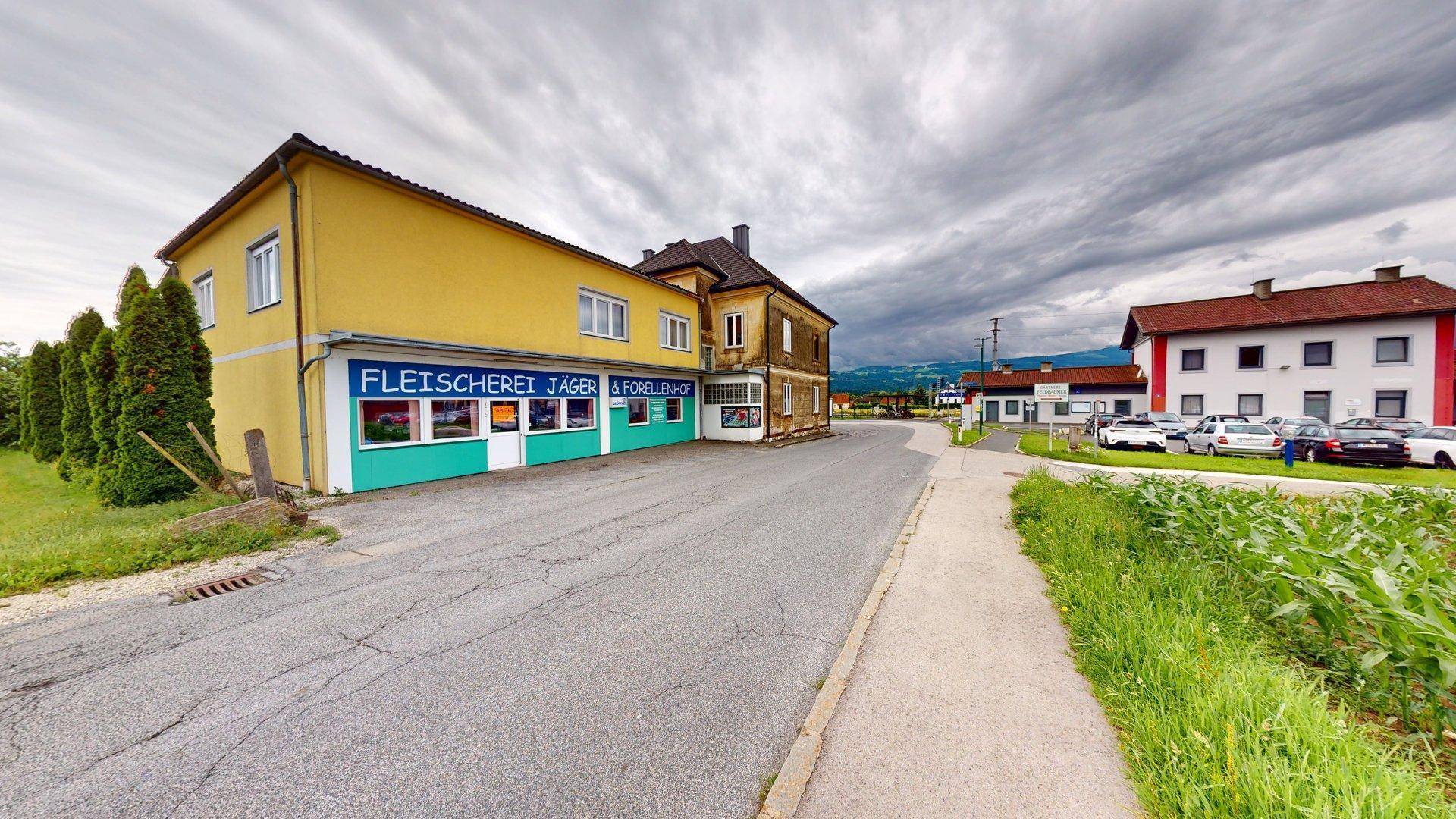 Straßenansicht mit einem gelben Gebäude, das eine Metzgerei beherbergt, und weiteren Häusern im Hintergrund.