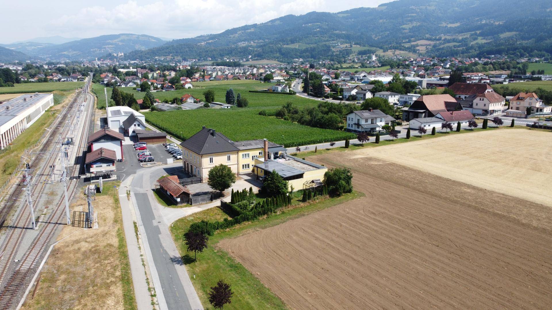 Luftaufnahme des Anwesens mit weiten Feldern, Bahngleisen und einer malerischen Berglandschaft im Hintergrund.