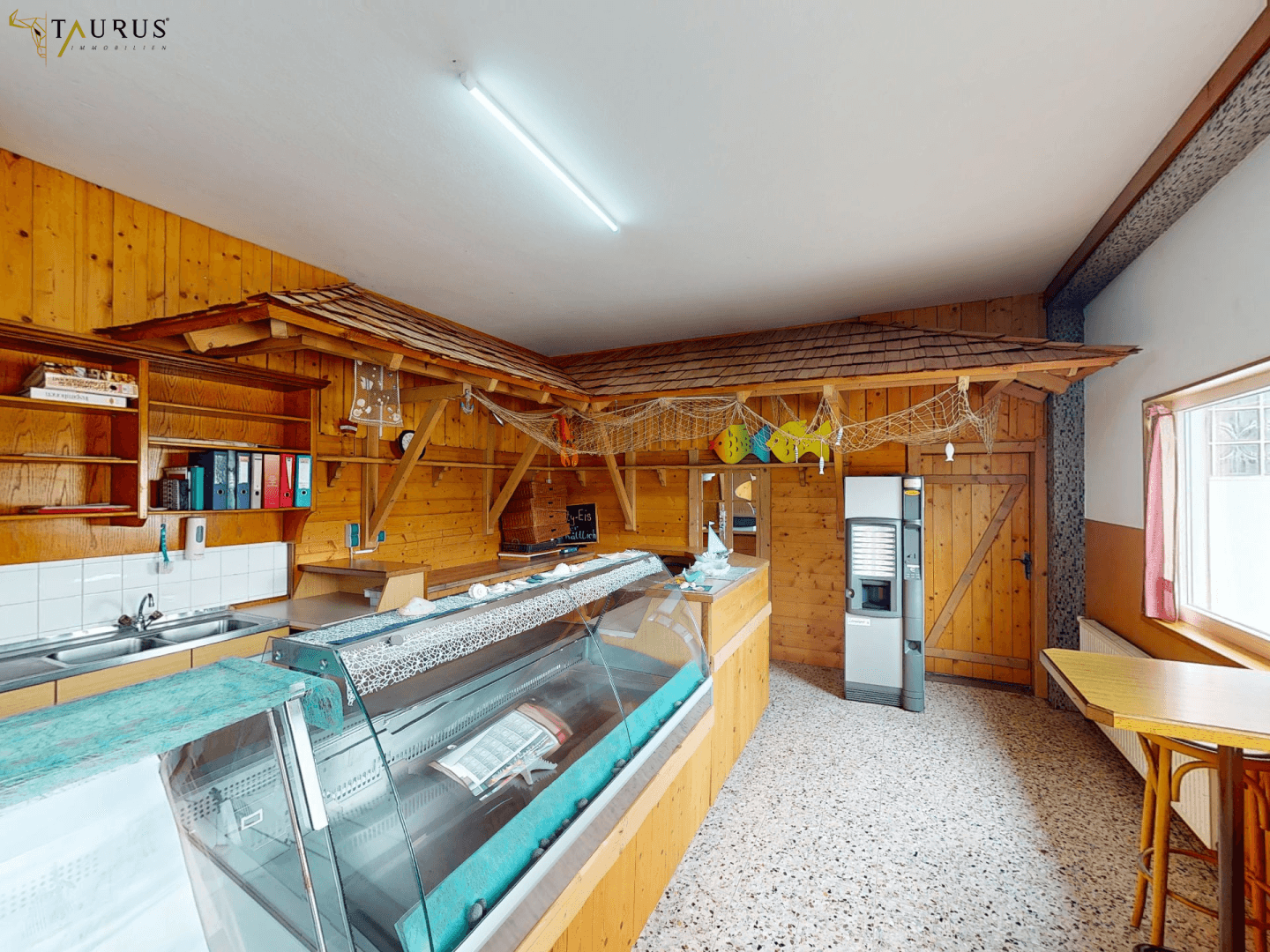 Verkaufsraum mit Holzverkleidung, Theke und Fischereidekoration, inklusive Geldautomat.