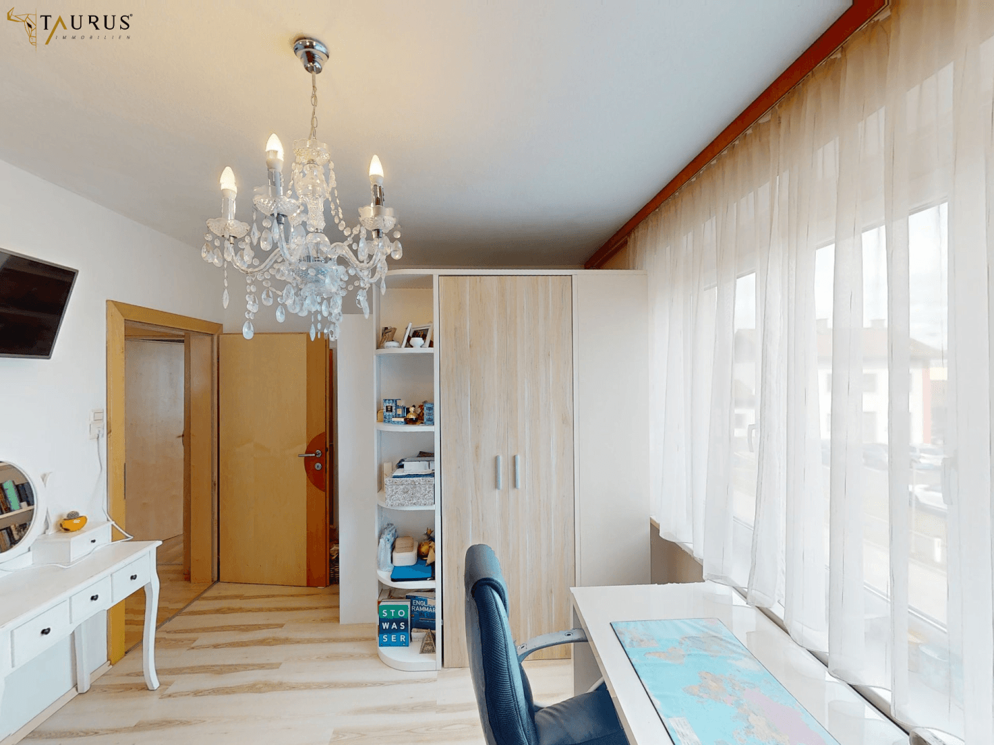 Freundliches Zimmer mit großem Fenster, Schreibtisch und einem Kleiderschrank, gut beleuchtet.