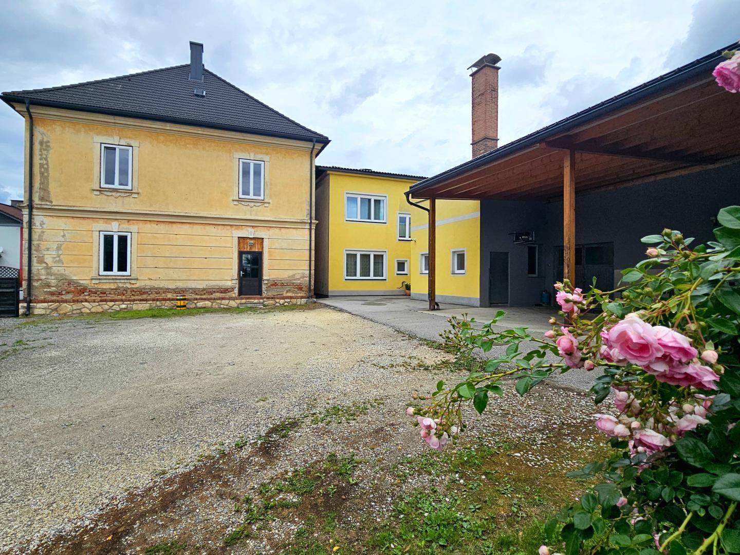 Außenansicht von zwei gelben Gebäuden mit einem Schotterhof und blühenden Rosen im Vordergrund.