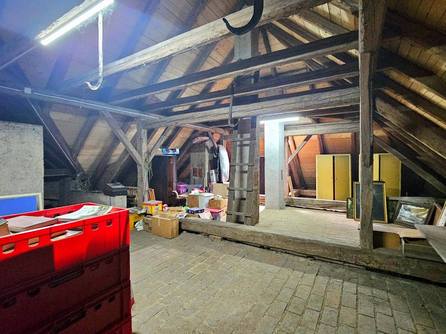 Geräumiger Dachboden mit sichtbaren Holzbalken und Ziegelboden, viel Stauraum.