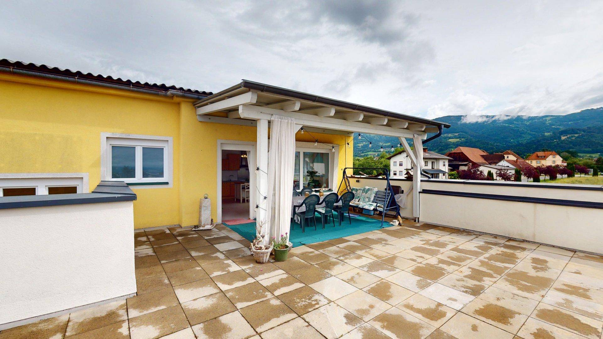 Große geflieste Terrasse mit Überdachung, Gartenmöbeln und Blick auf die umliegende Landschaft.