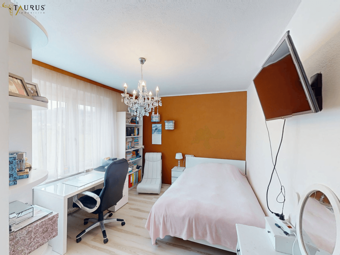 Helles Zimmer mit Schreibtisch, Einzelbett und einem Kronleuchter, ideal als Schlaf- oder Arbeitszimmer.
