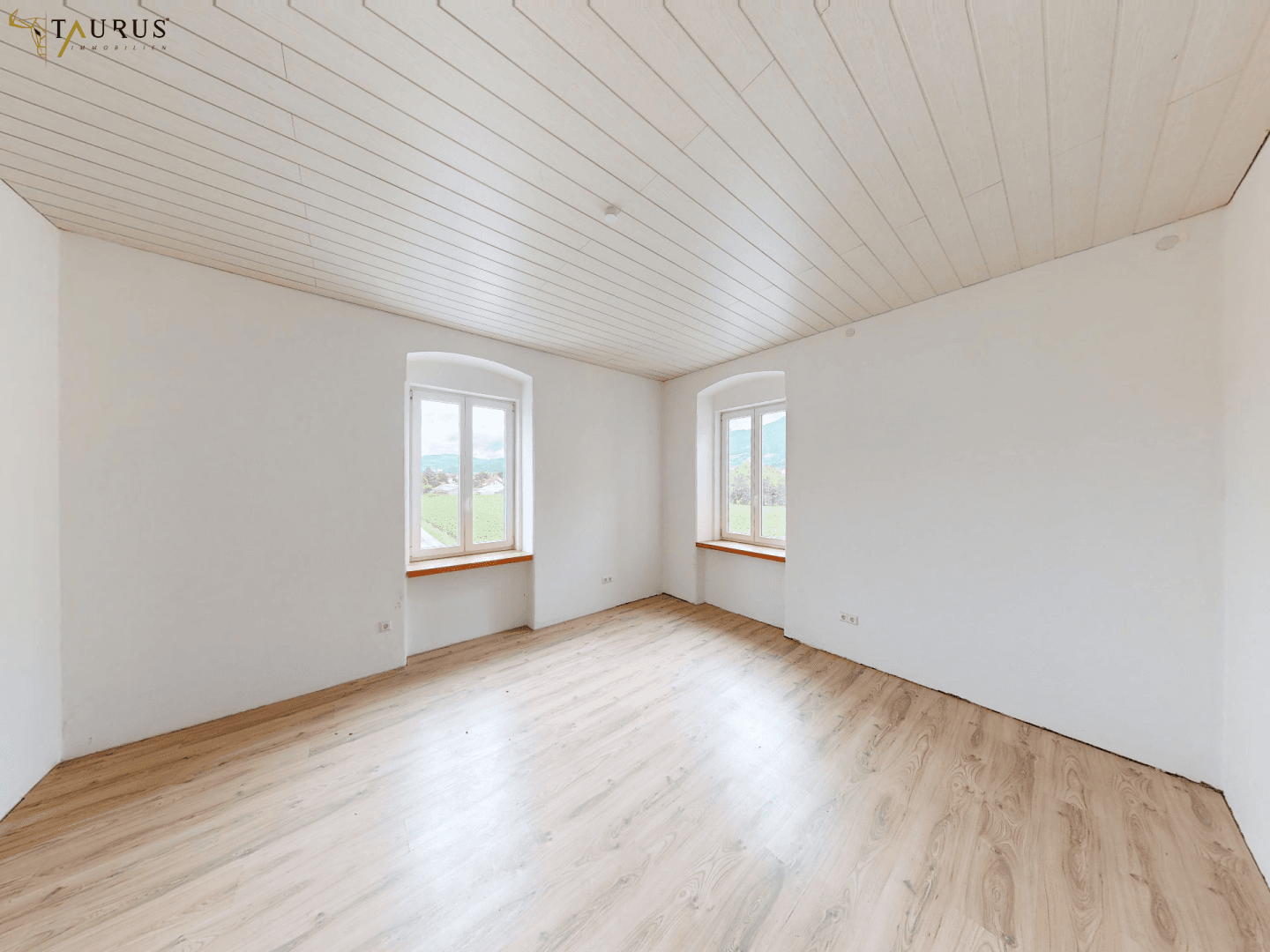 Helles, renoviertes Zimmer mit neuem Laminatboden und Holzdeckenverkleidung, Blick ins Grüne.