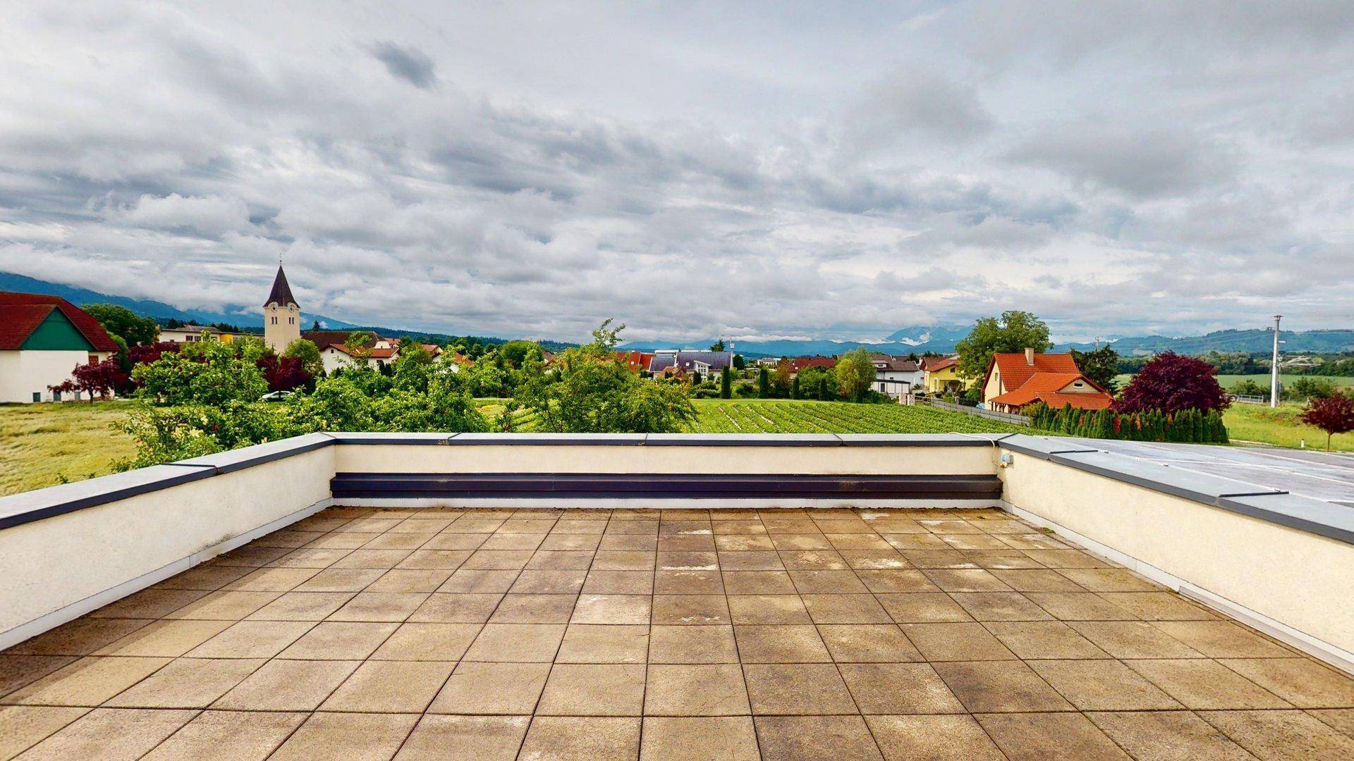 Große Dachterrasse mit Fliesenboden und weitem Blick über die Landschaft und umliegende Häuser.