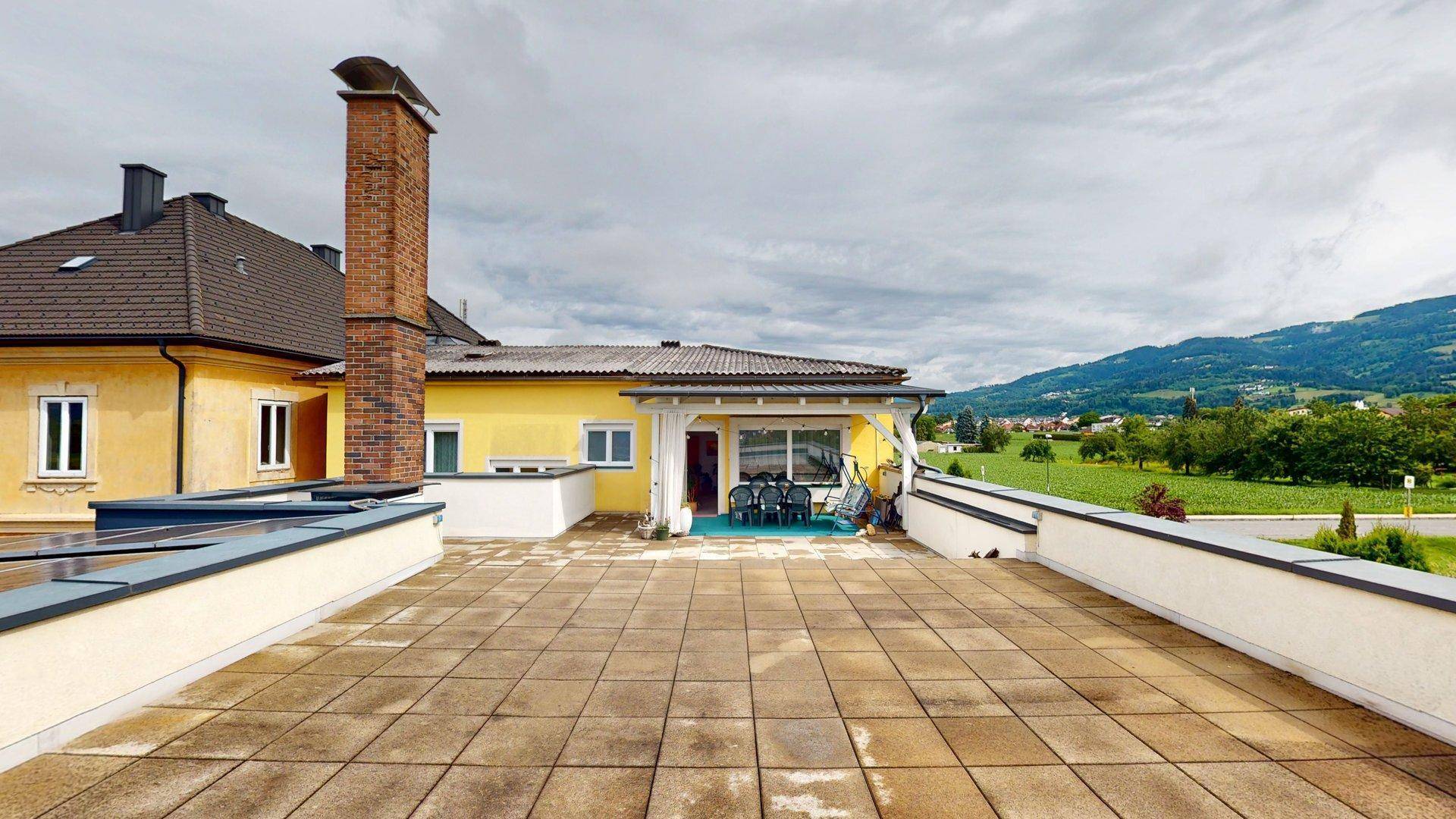 Weitläufige Dachterrasse mit Fliesenboden und Panoramablick auf die grüne Hügellandschaft.