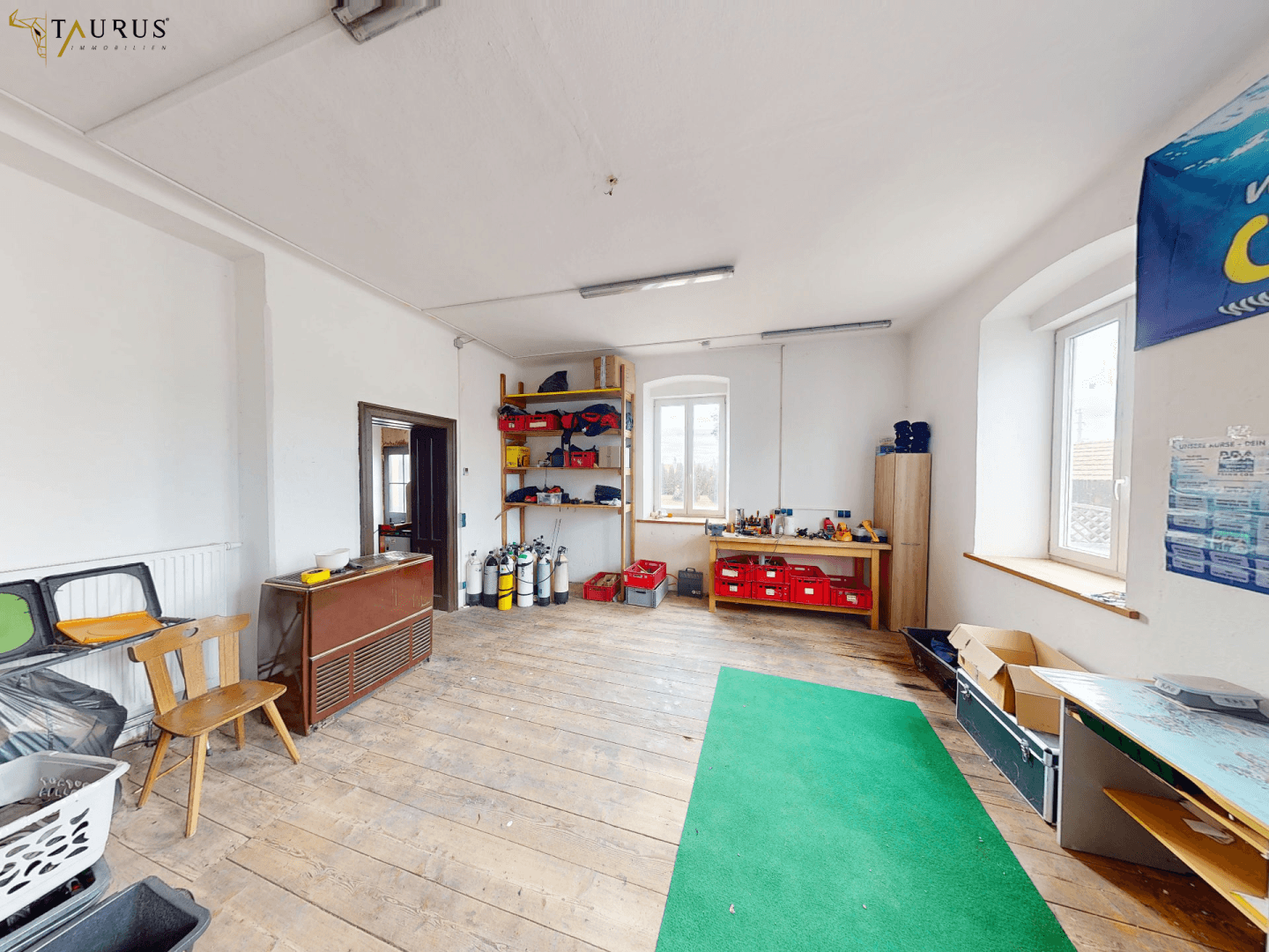 Großer Raum mit Holzboden, Regalen und Arbeitsmaterialien, ideal als Werkstatt oder Büro.