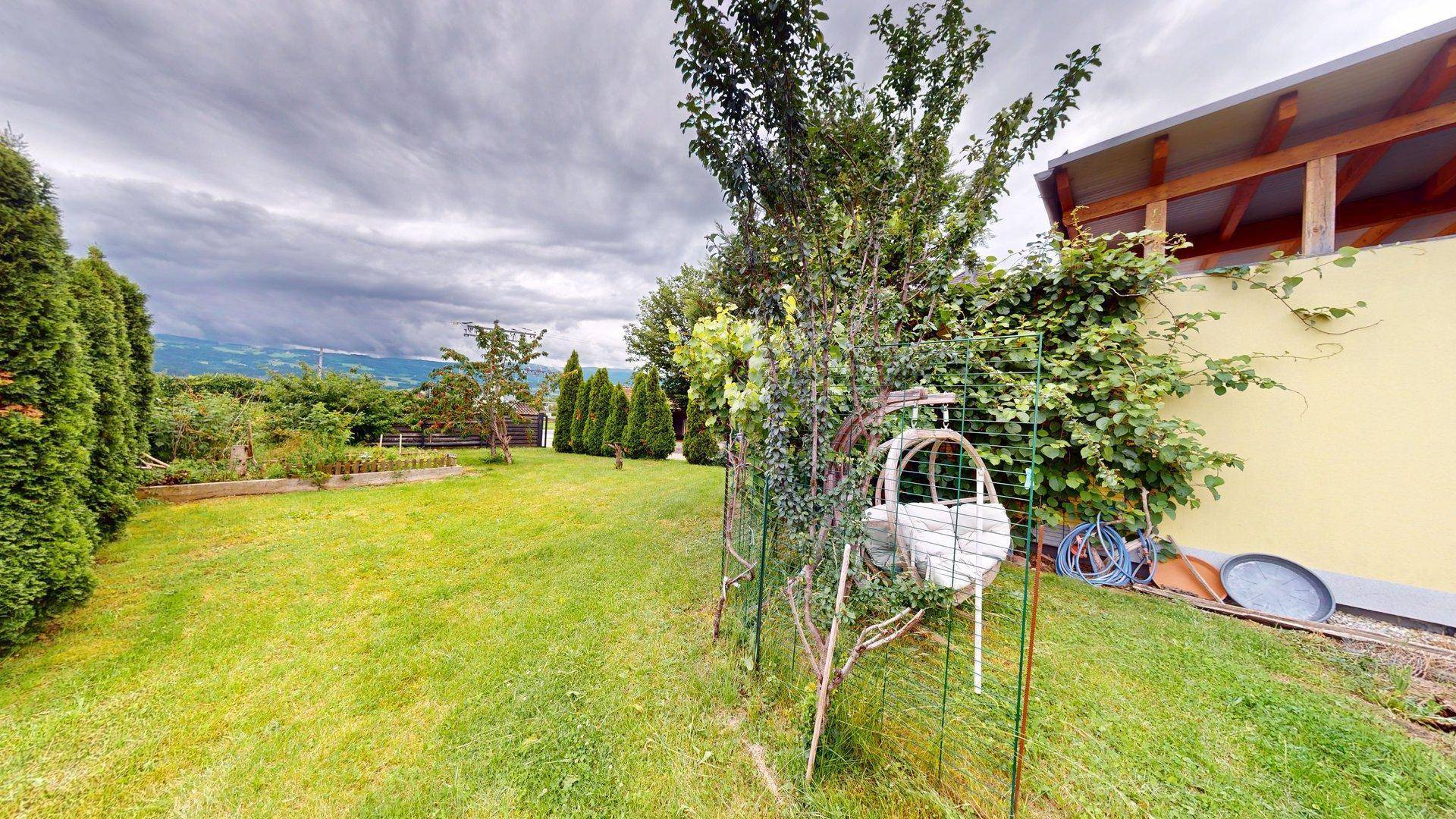 Weitläufiger Garten mit gepflegtem Rasen, Bäumen und Sträuchern sowie Bergblick in der Ferne.