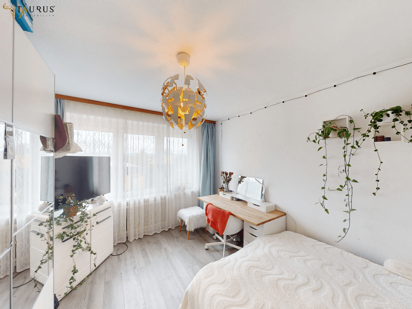 Helles Schlafzimmer mit modernem Bett, Schreibtisch und einem großen Fenster mit Vorhängen.
