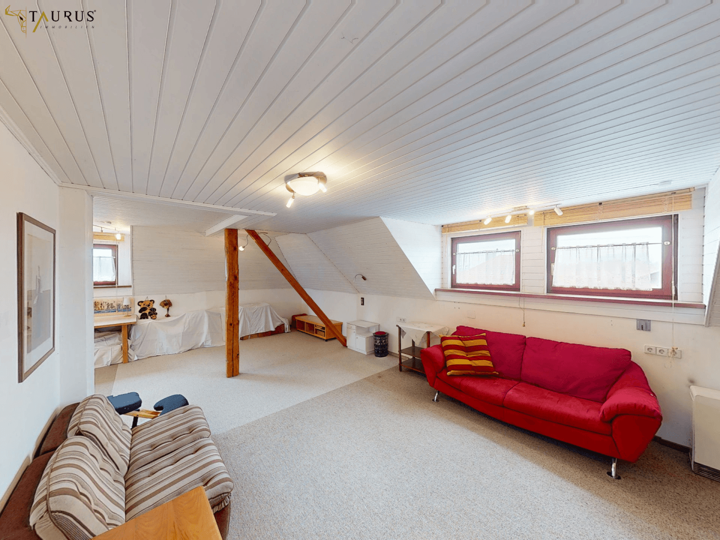 Gemütliches Dachgeschoss-Wohnzimmer mit schrägen Wänden, Teppichboden und bequemen Sofas.