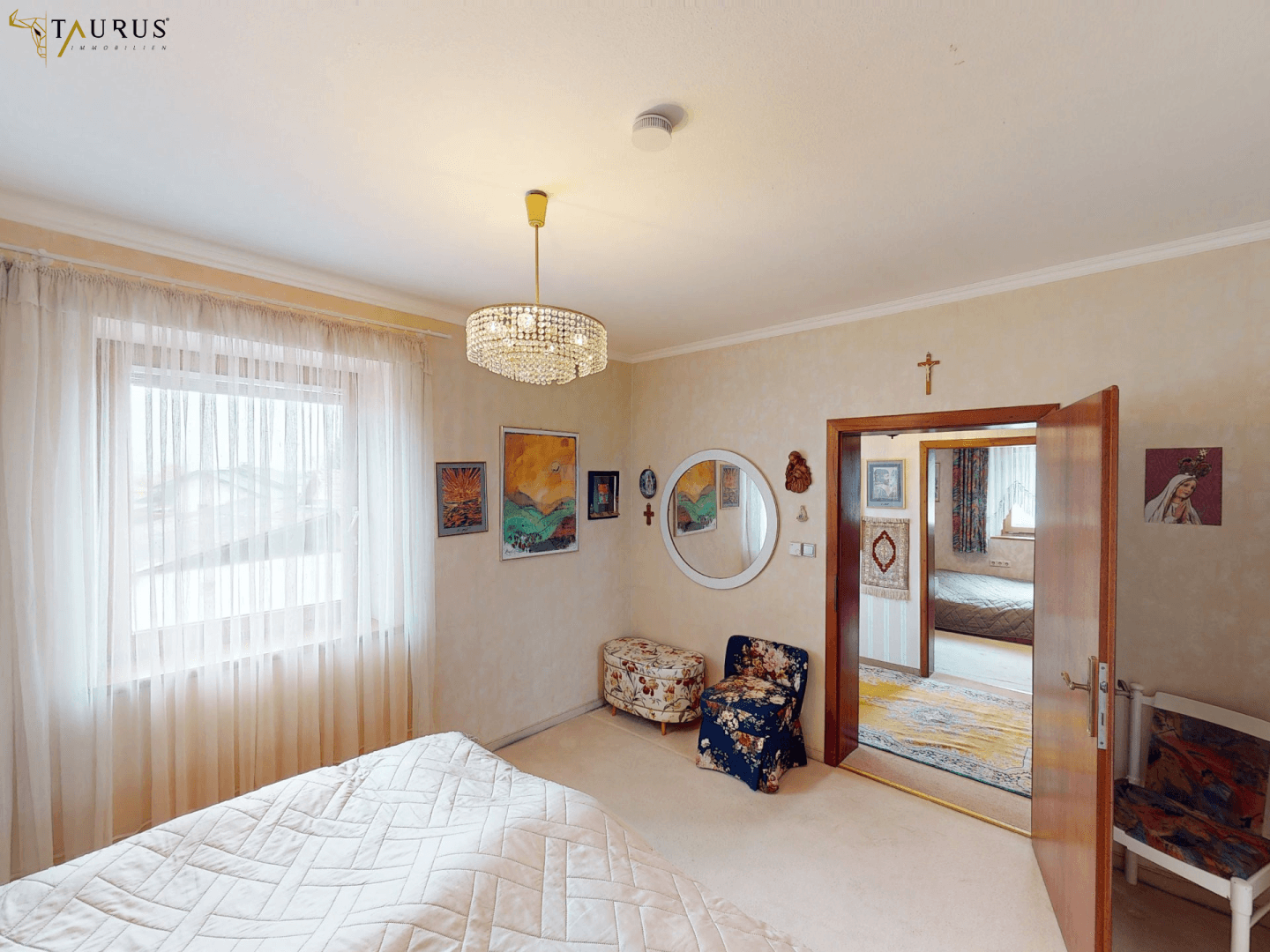 Helles Schlafzimmer mit Teppichboden, Kronleuchter und Zugang zu einem weiteren Raum.