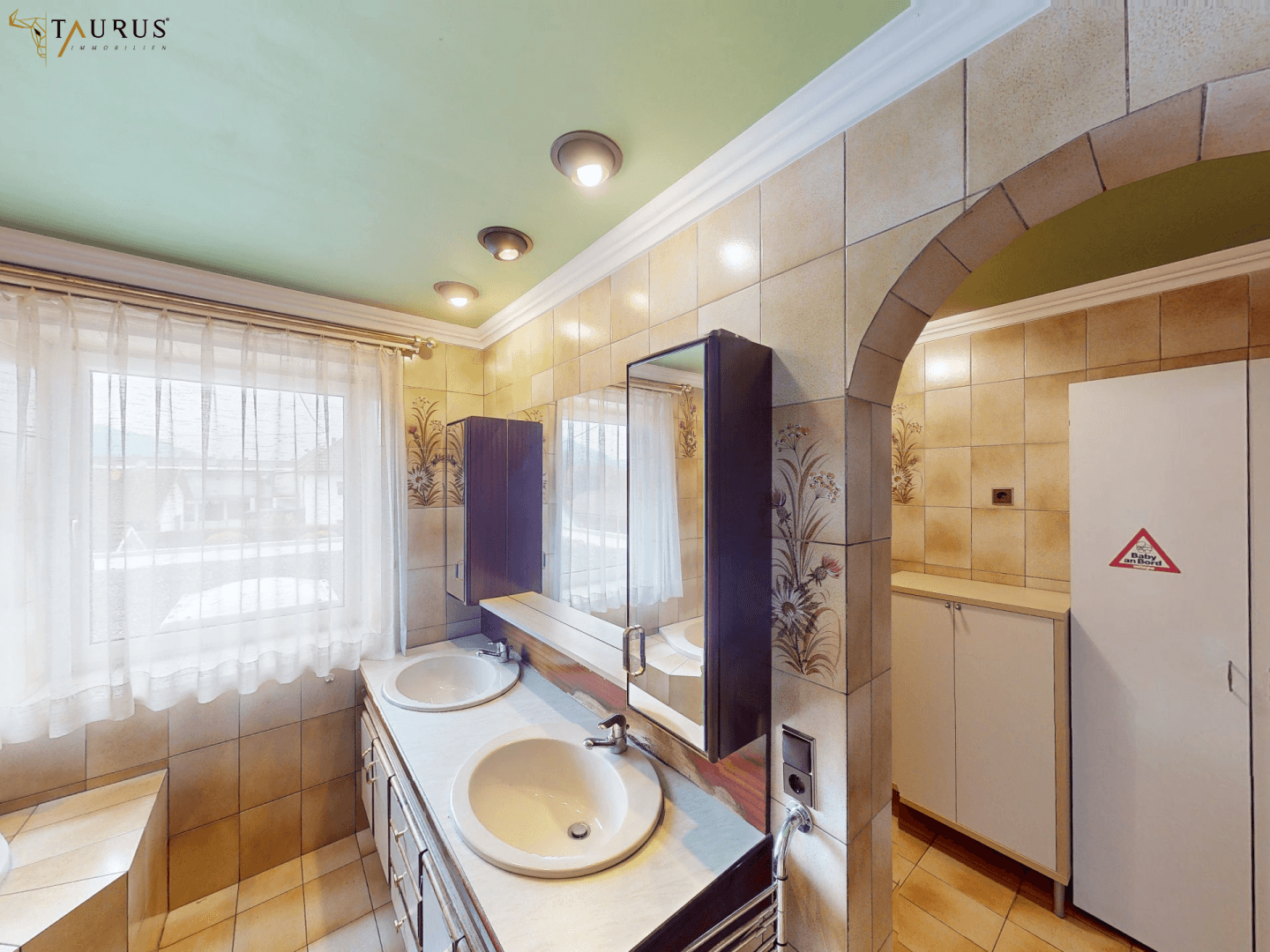 Badezimmer mit Doppelwaschbecken, Spiegelschrank und gemusterten Fliesen.