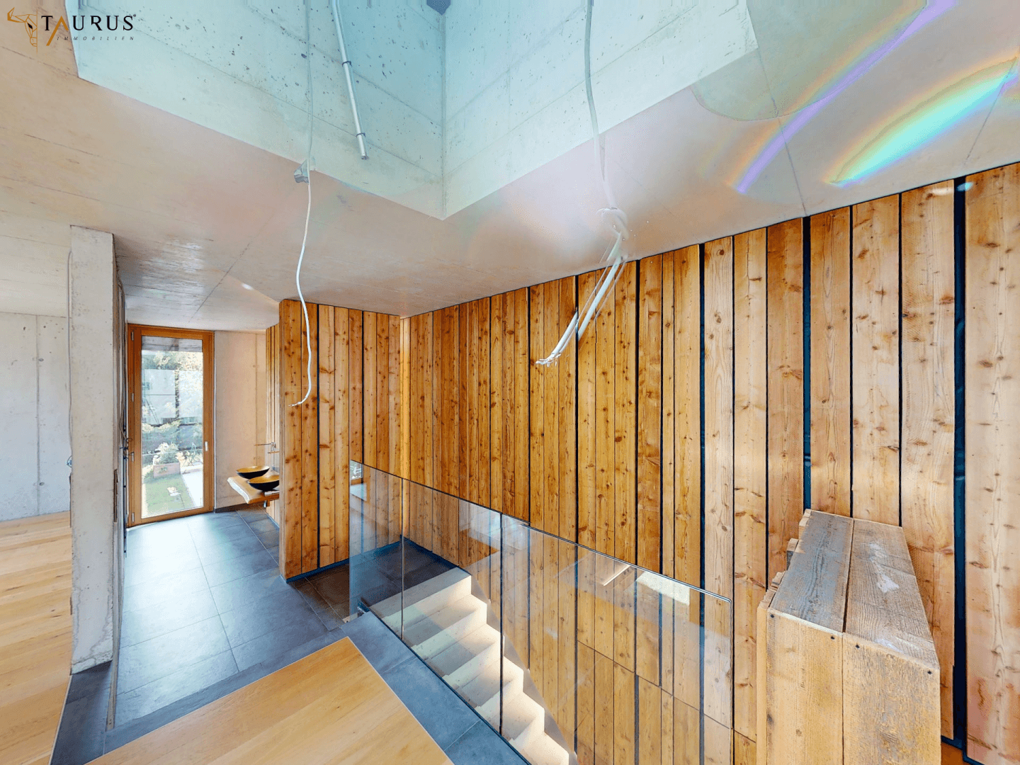 Moderner Treppenbereich mit Holzverkleidung, Glasgeländer und Sichtbetondecke.
