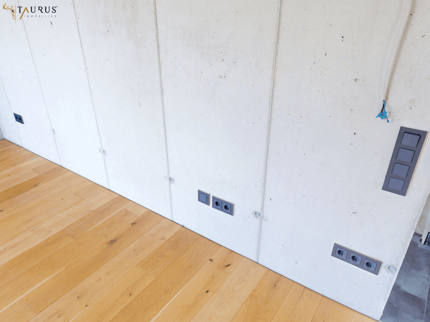 Detailaufnahme einer Sichtbetonwand mit Steckdosen und Holzboden.