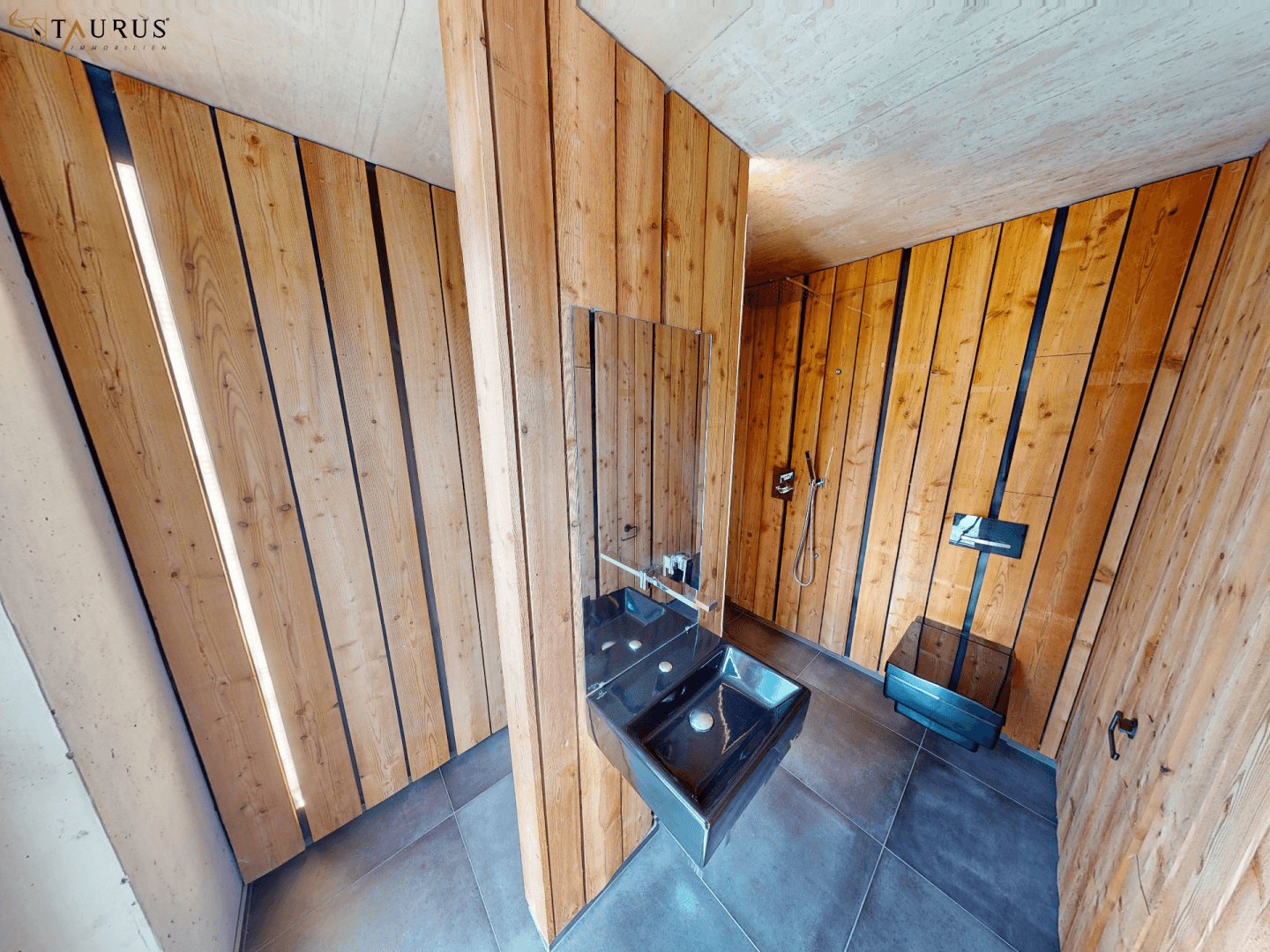 Modernes Badezimmer mit Holzverkleidung, dunklen Fliesen und minimalistischem Waschbecken.