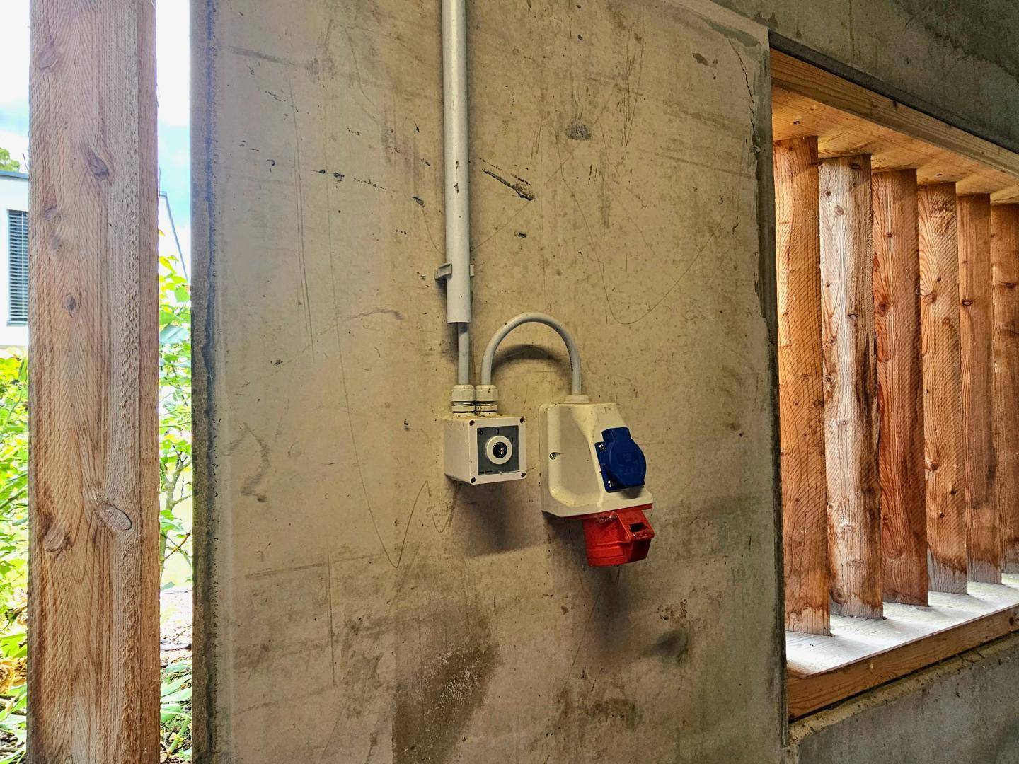 Detailansicht einer Betonwand mit Steckdosen und Holzlamellen im Hintergrund.
