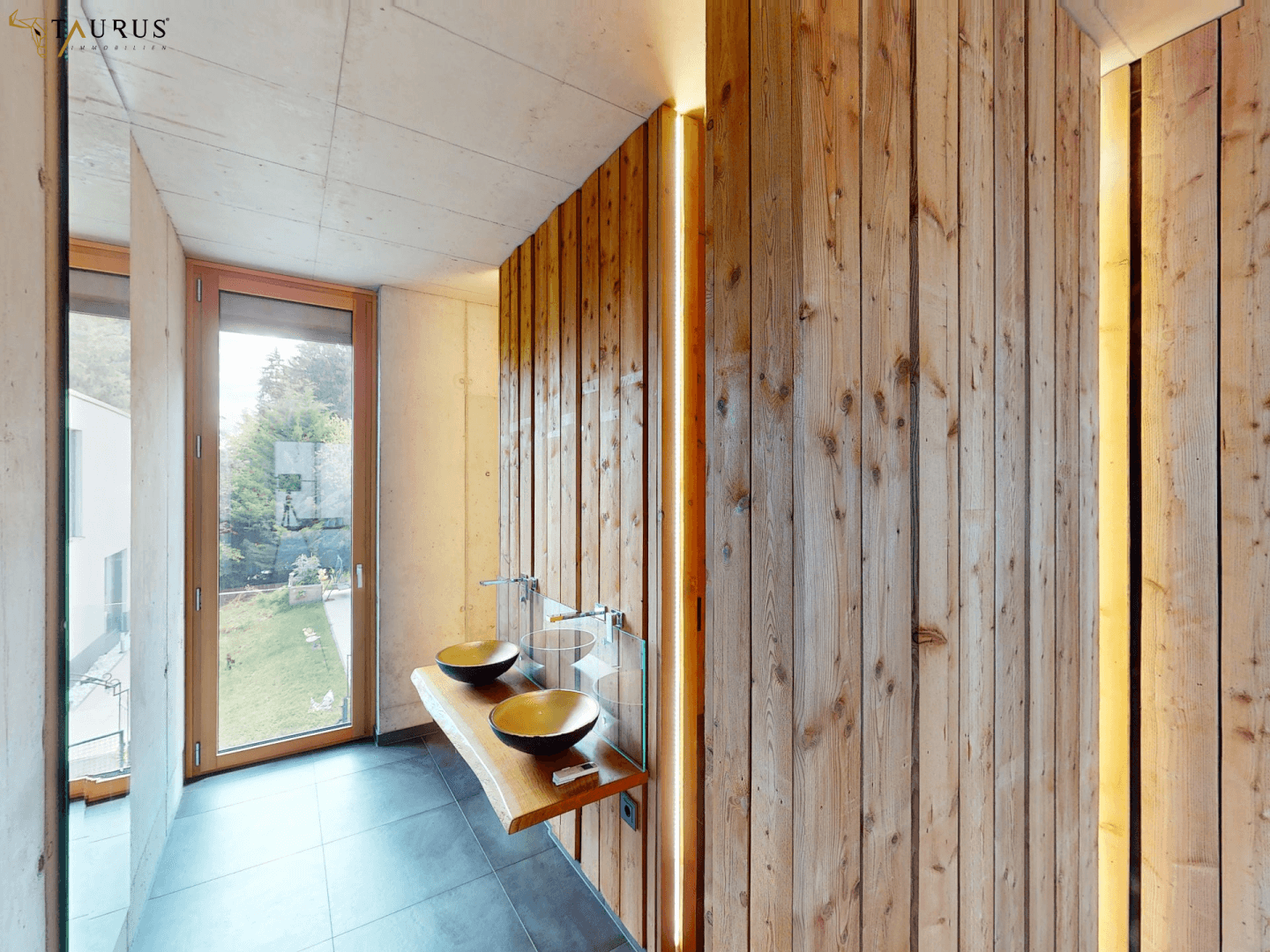 Modernes Badezimmer mit Holzverkleidung, zwei Waschbecken und Fenster mit Blick ins Grüne.