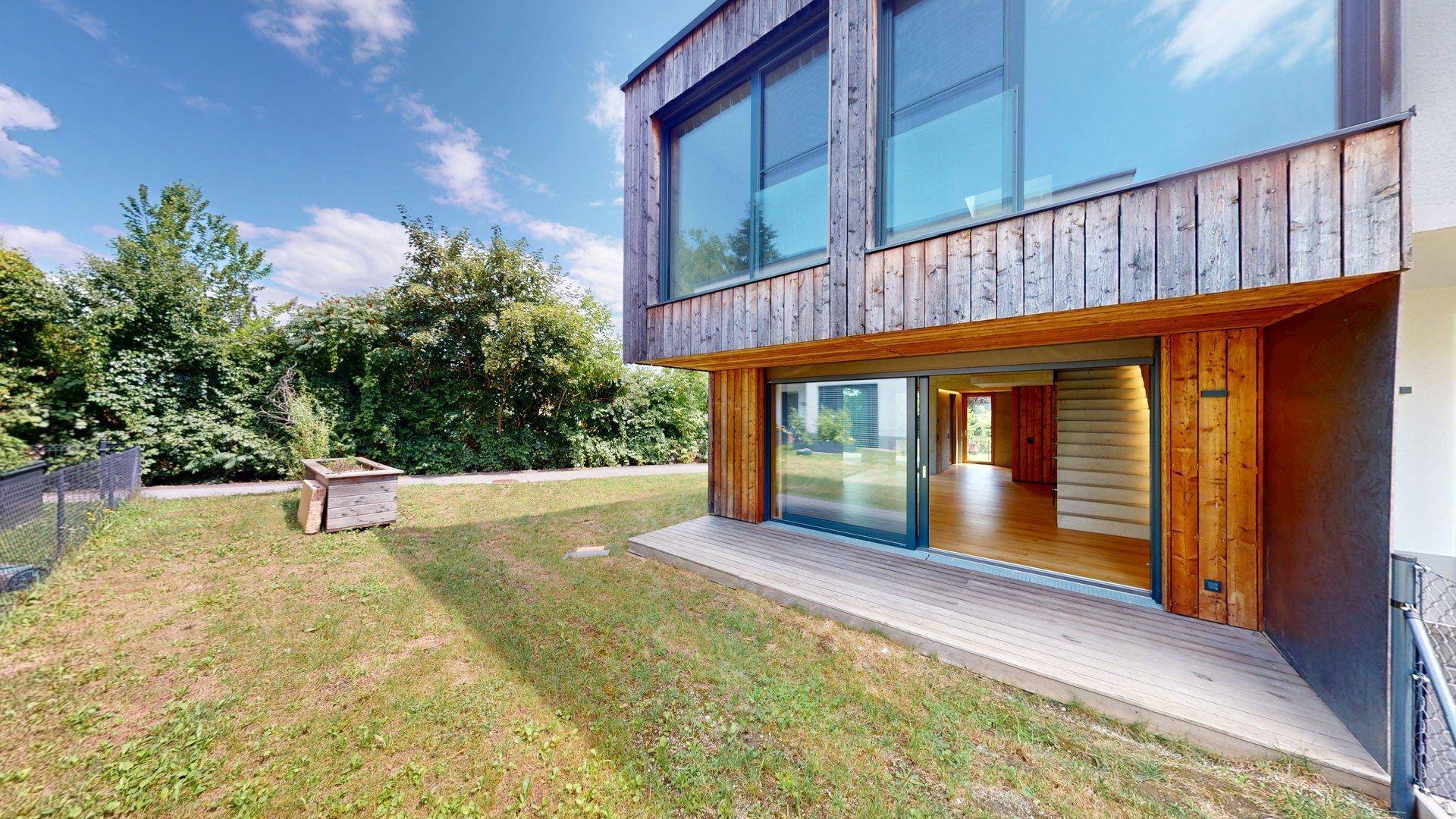 Gartenbereich mit Holzterrasse und großen Schiebetüren zum Innenraum des modernen Hauses.