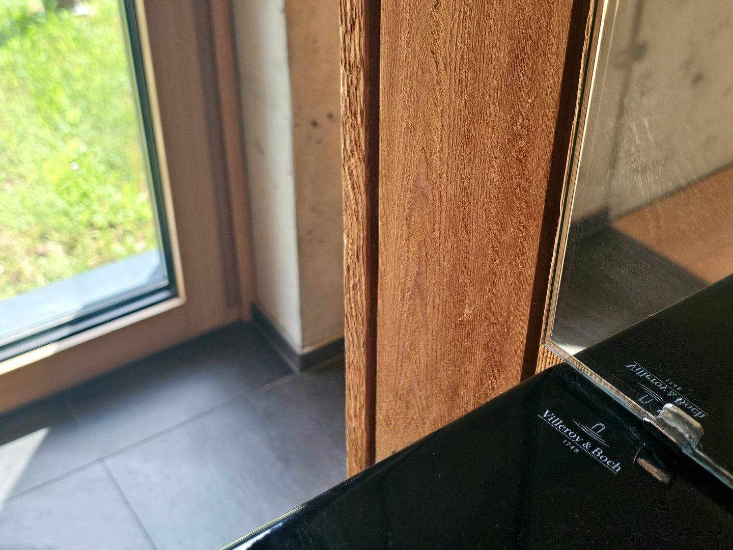 Detailaufnahme des modernen Waschbeckens mit dunklen Fliesen und Fensterblick ins Grüne.