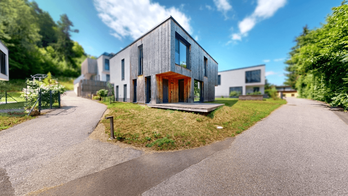 Modernes Wohnhaus mit Holzfassade und Zufahrt in einer naturnahen Siedlung.