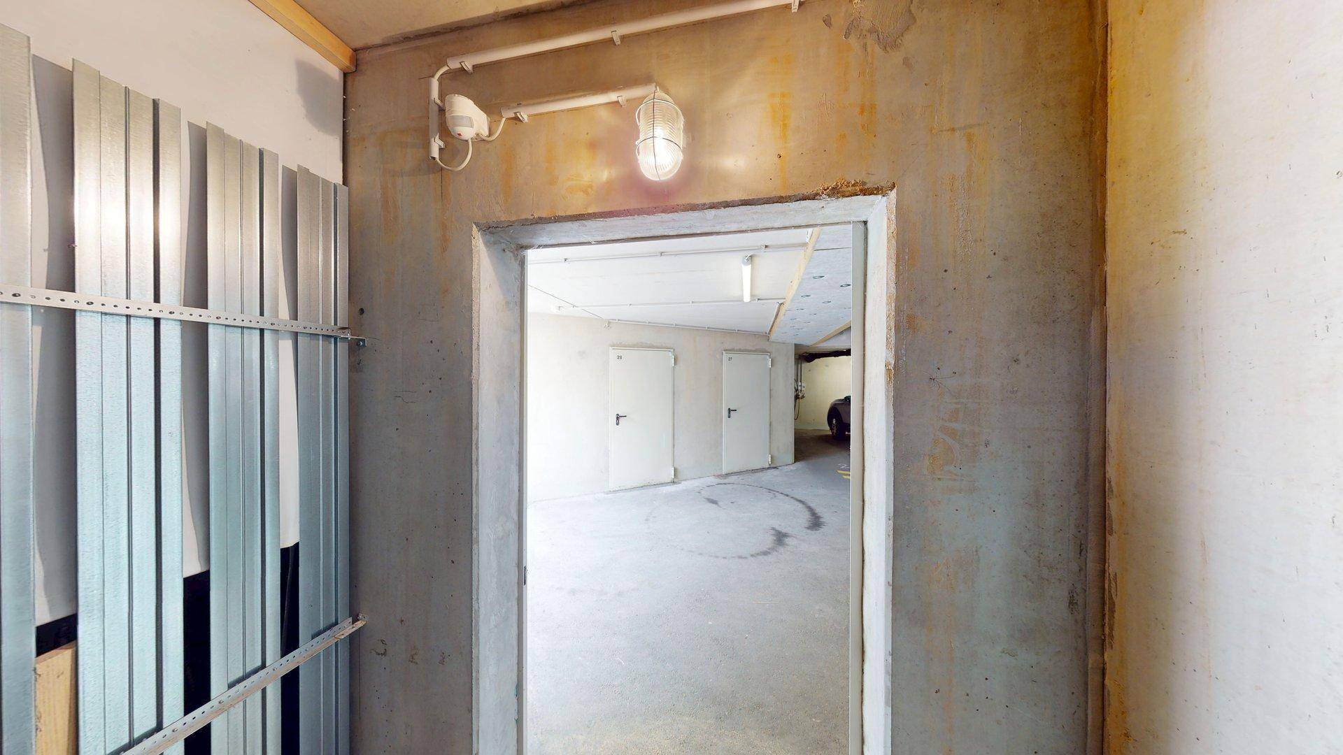 Eingang zu einem Kellerraum mit Betonwänden und einfacher Beleuchtung.
