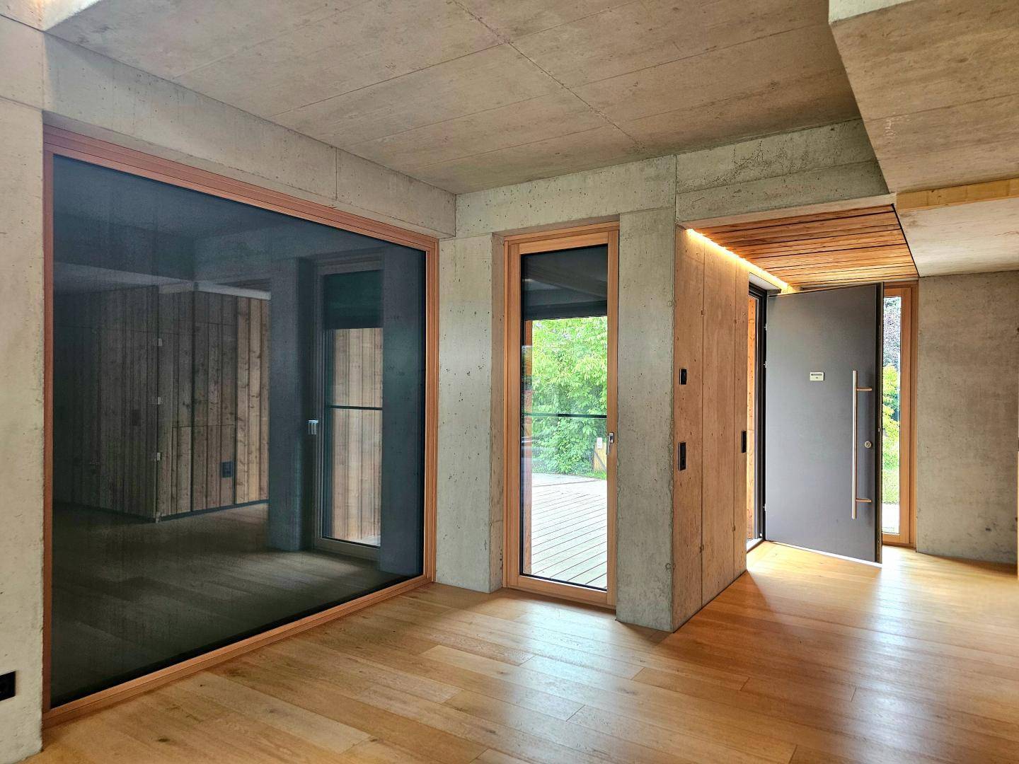 Eingangsbereich mit Holzboden, Sichtbetonwänden und einer modernen Eingangstür.