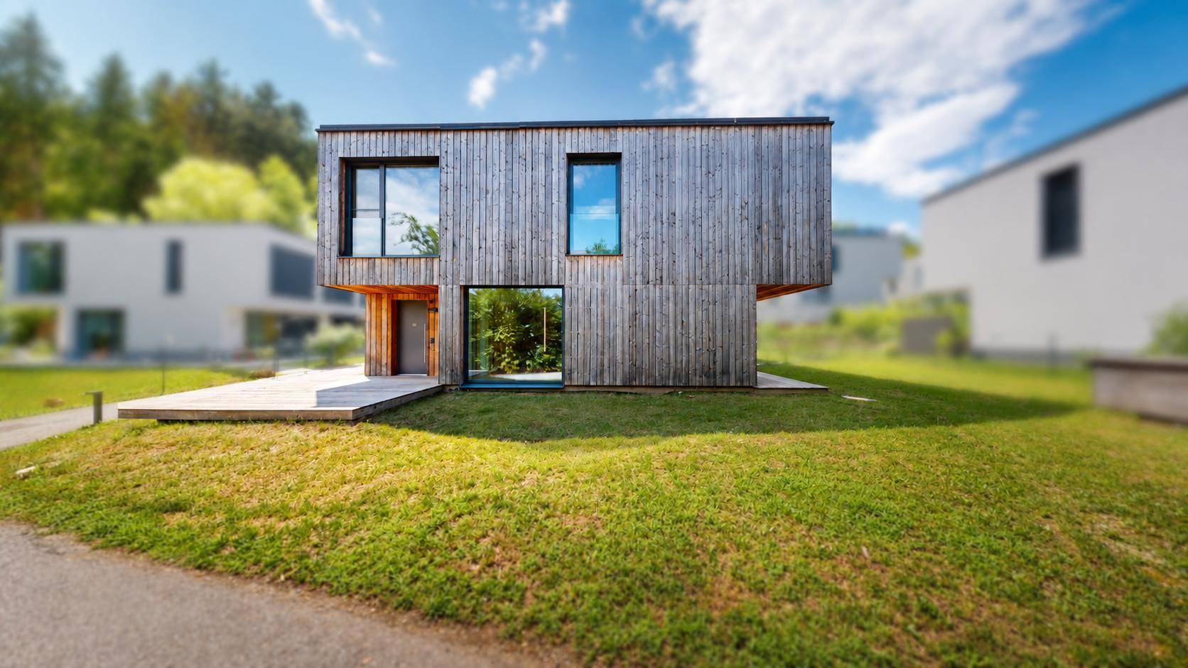 Freistehendes modernes Haus mit Holzfassade und kleiner Holzterrasse im Grünen.